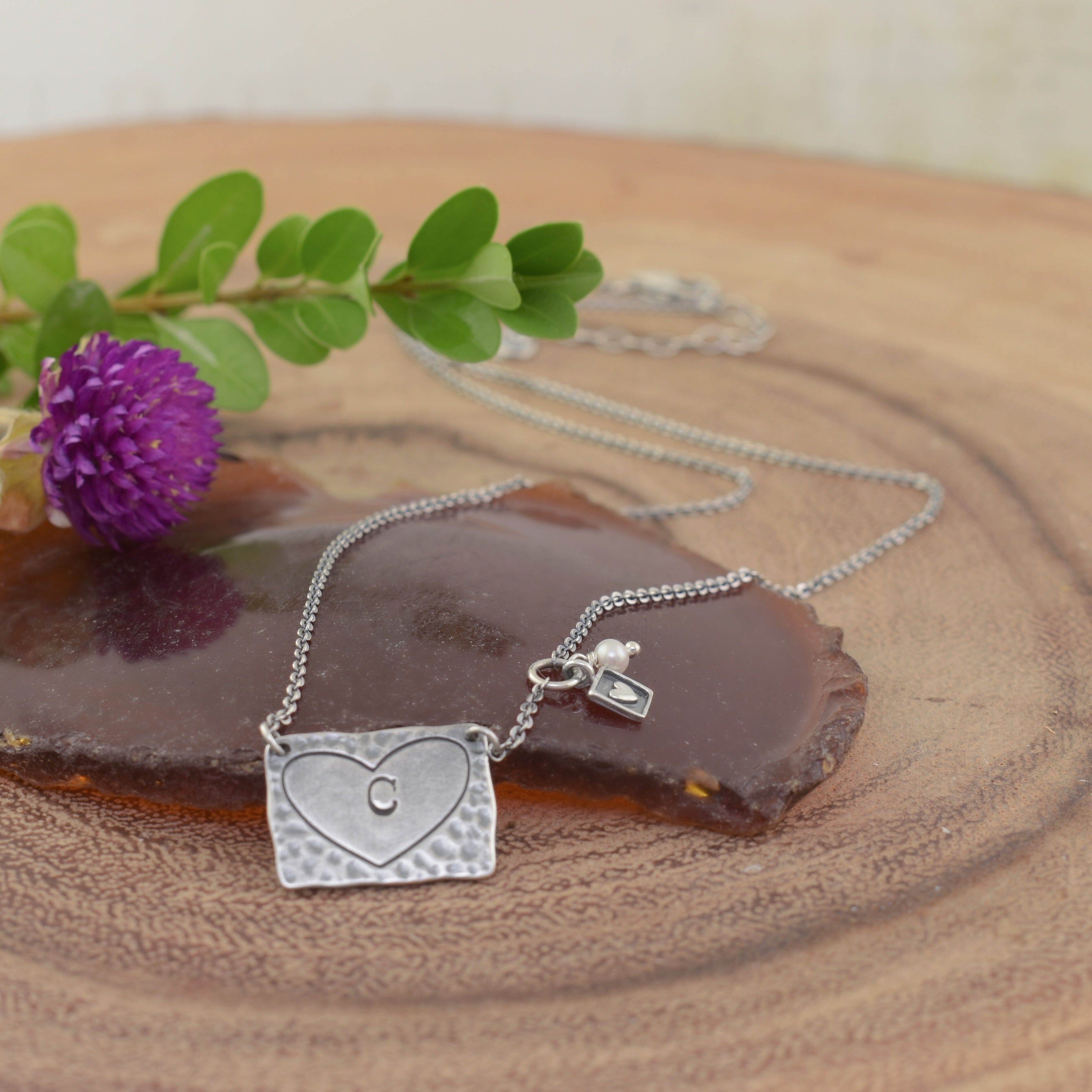 A sterling silver heart-shaped pendant necklace with a small initial 'C' engraved in the center