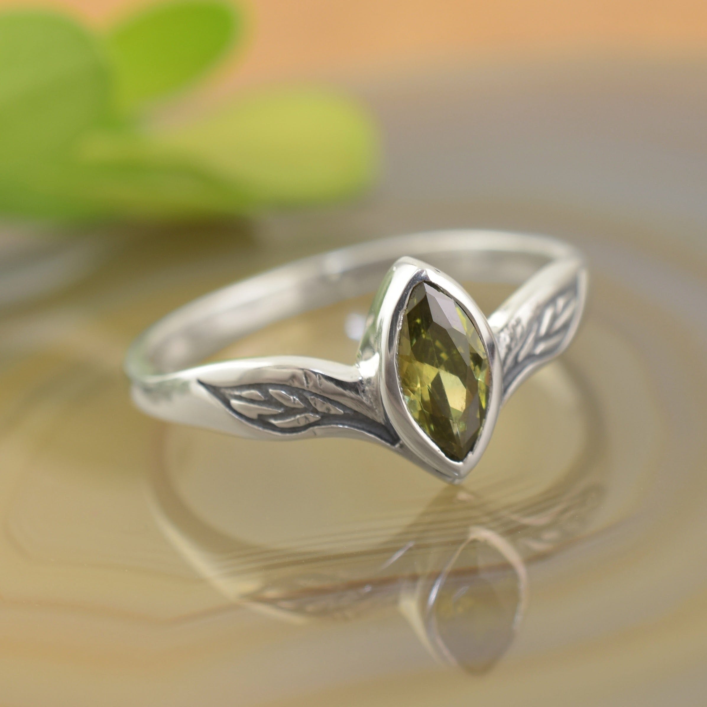 A sterling silver ring with a marquise-cut olive-green CZ in the center with engraved leaf silhouettes on each side
