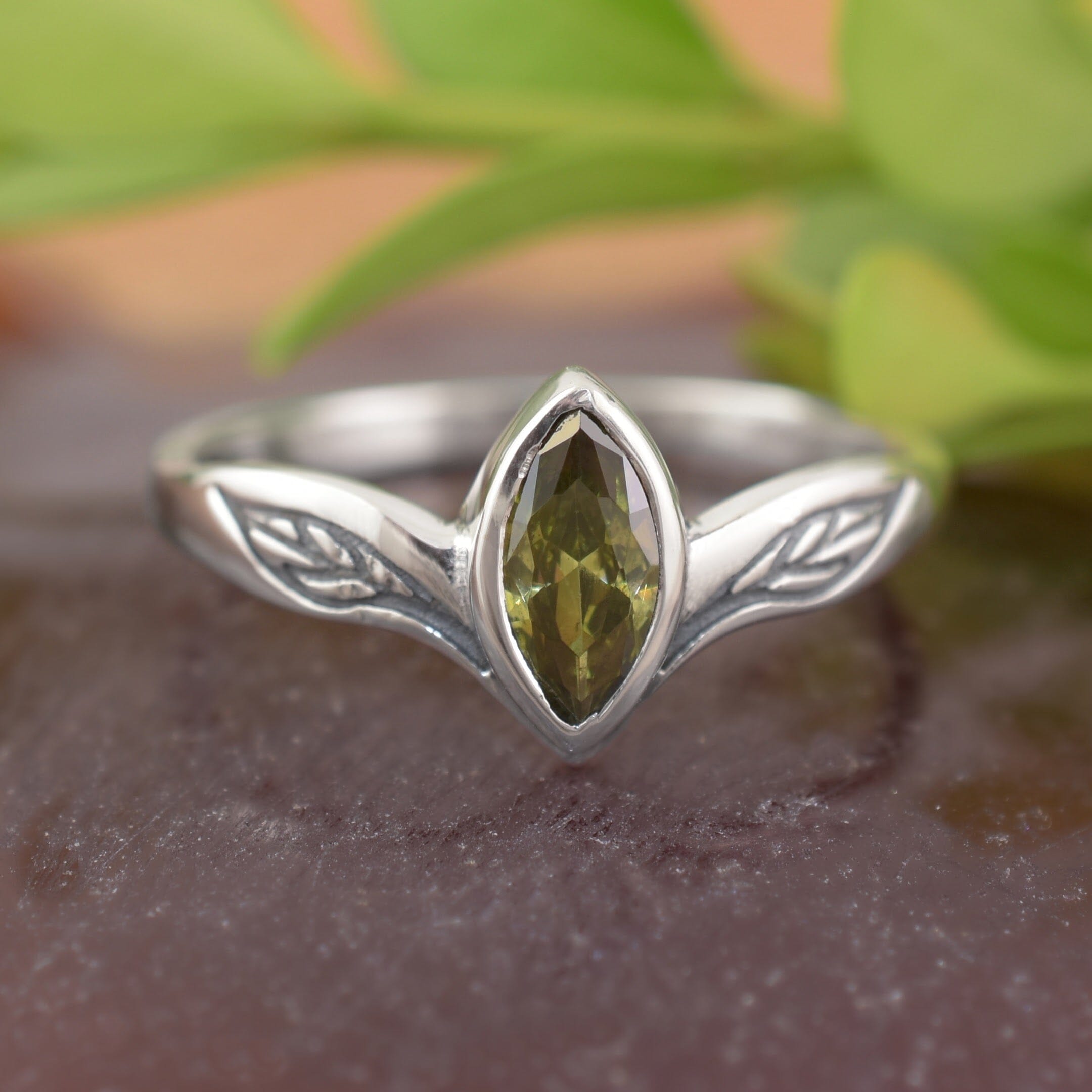 A sterling silver ring with a marquise-cut olive-green CZ in the center with engraved leaf silhouettes on each side