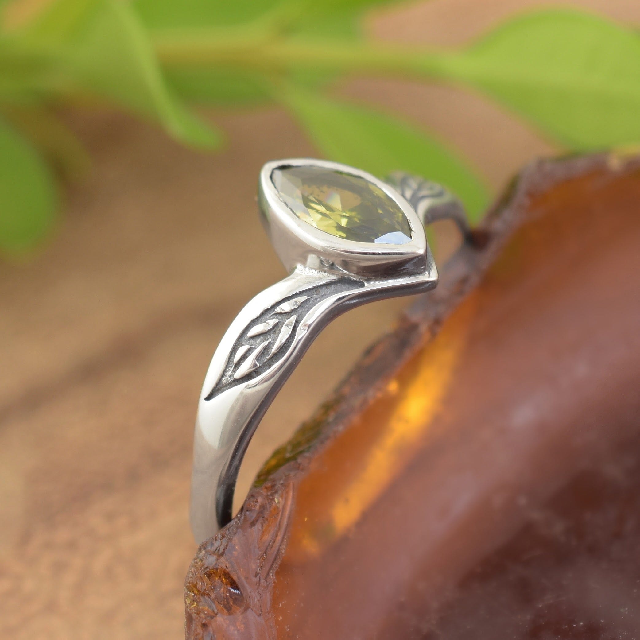 A sterling silver ring with a marquise-cut olive-green CZ in the center with engraved leaf silhouettes on each side
