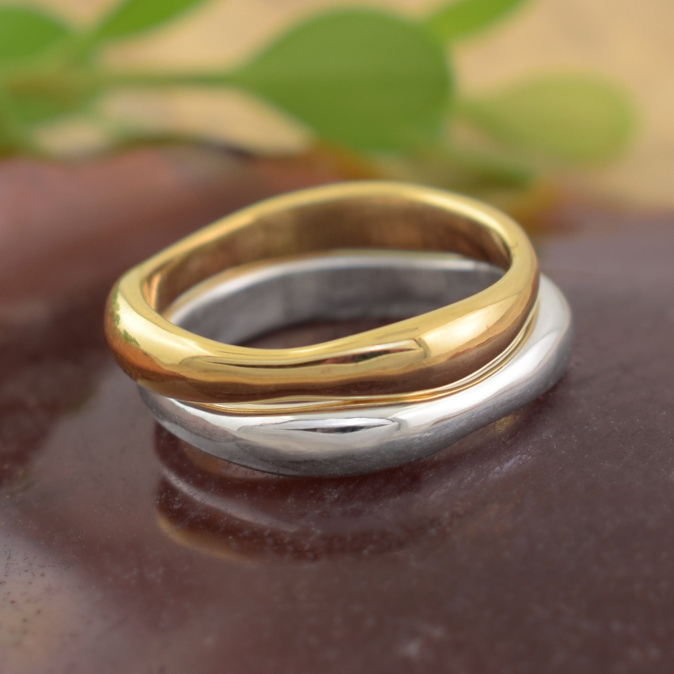 Two polished rings with a wavy, flowing design, featuring one polished gold band and one polished sterling silver band