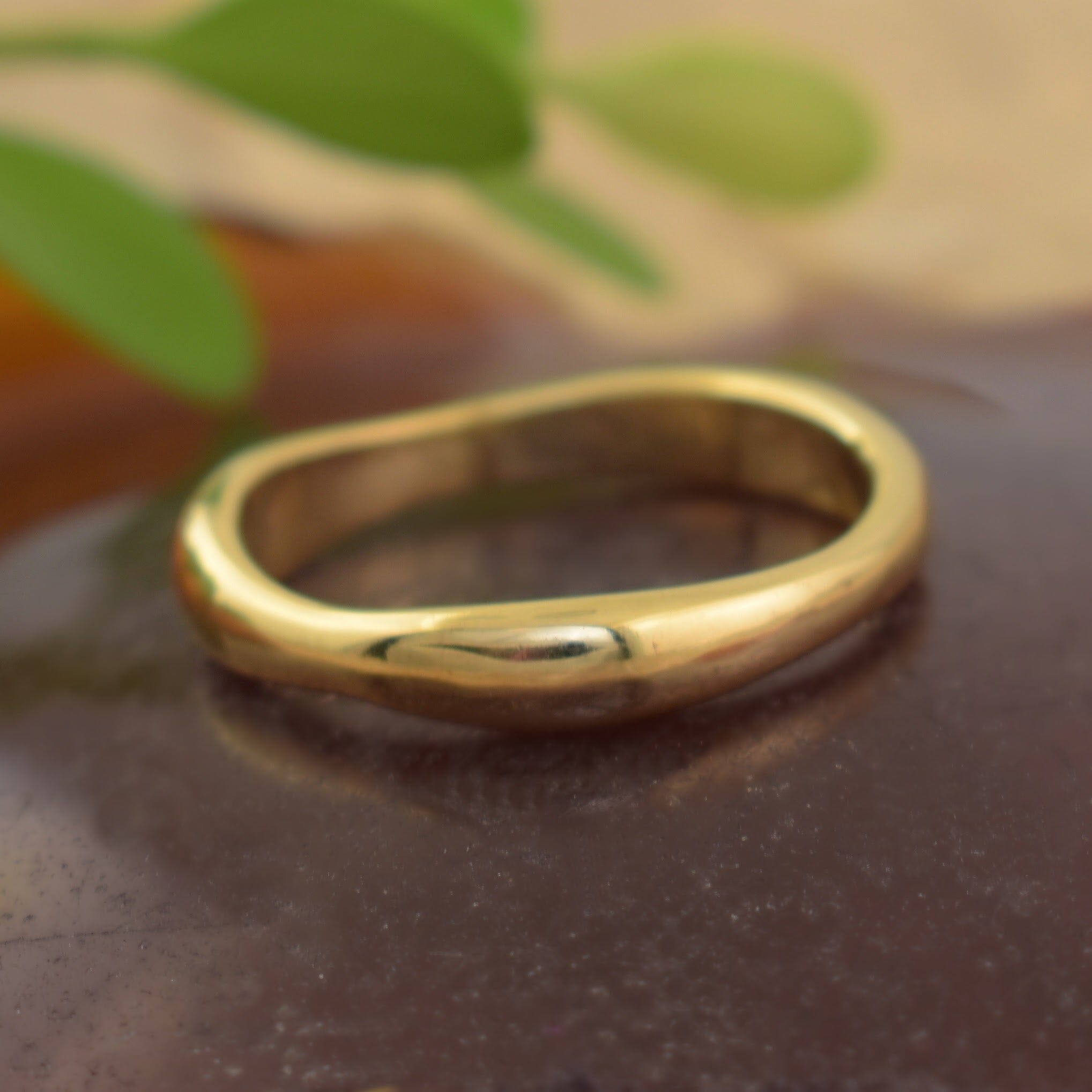 A polished gold ring with a smooth, organic wavy band
