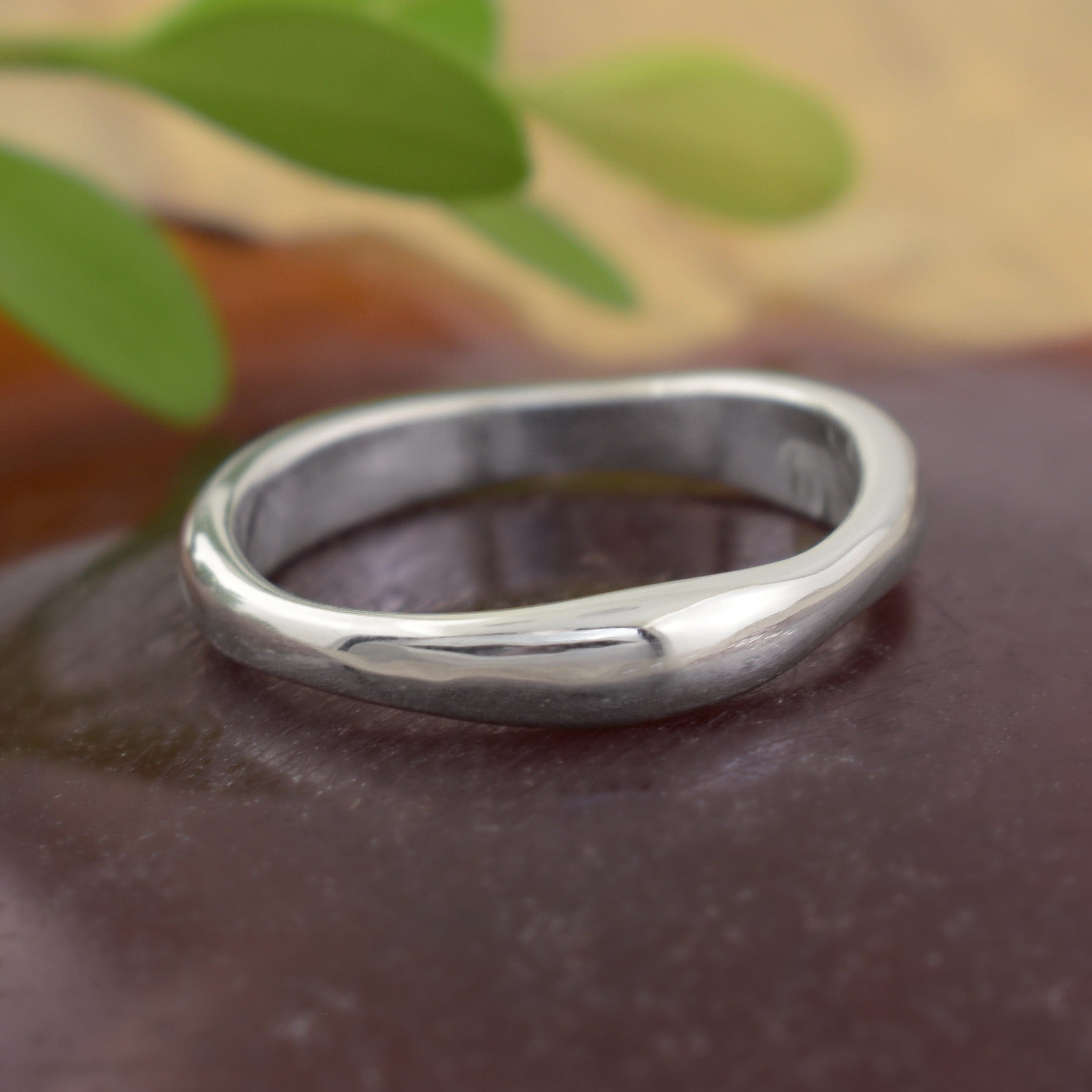 A polished sterling silver band ring with a smooth, organic wavy shape