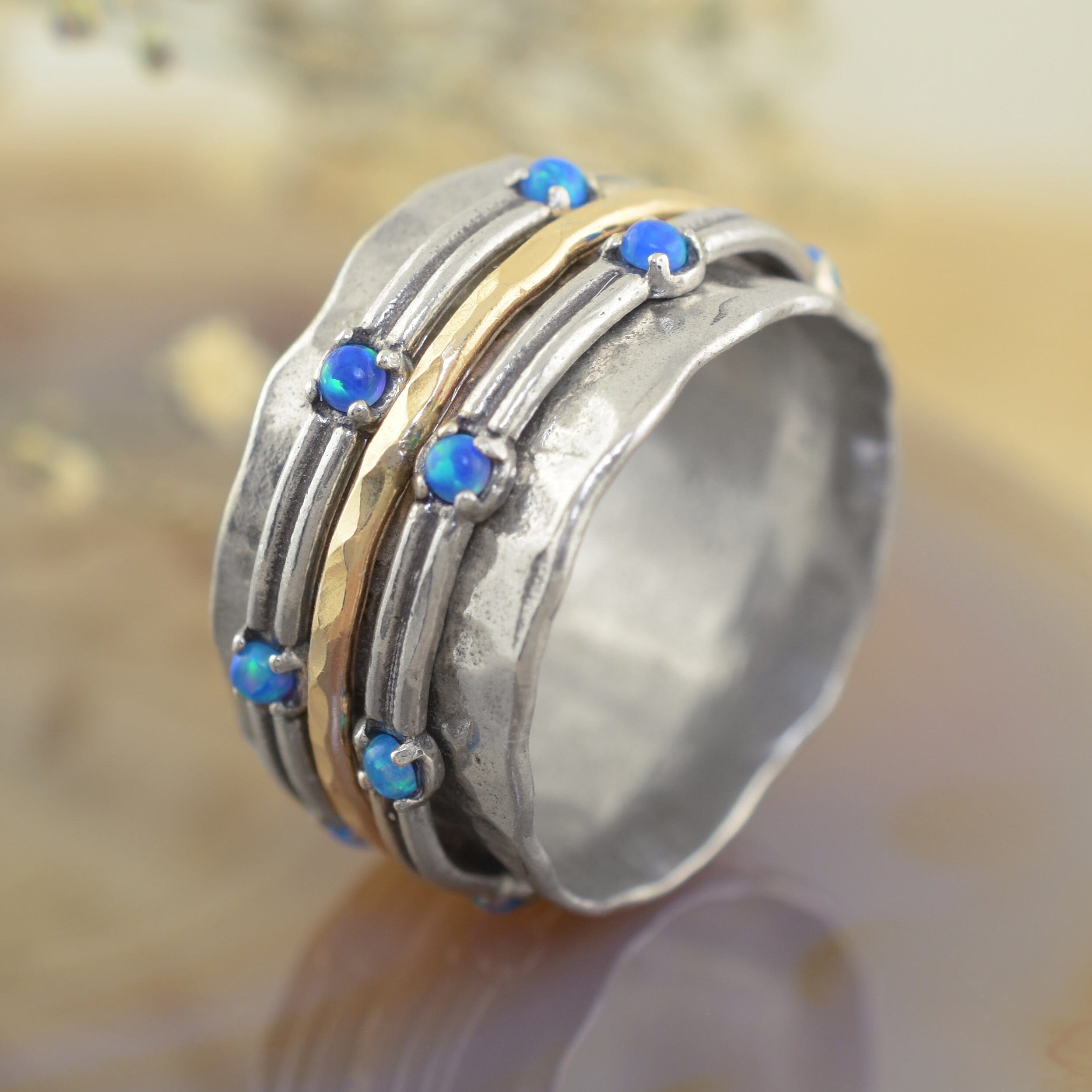 A sterling silver band ring with multiple textured grooves, a central gold band, and small blue opal gemstones set along the front