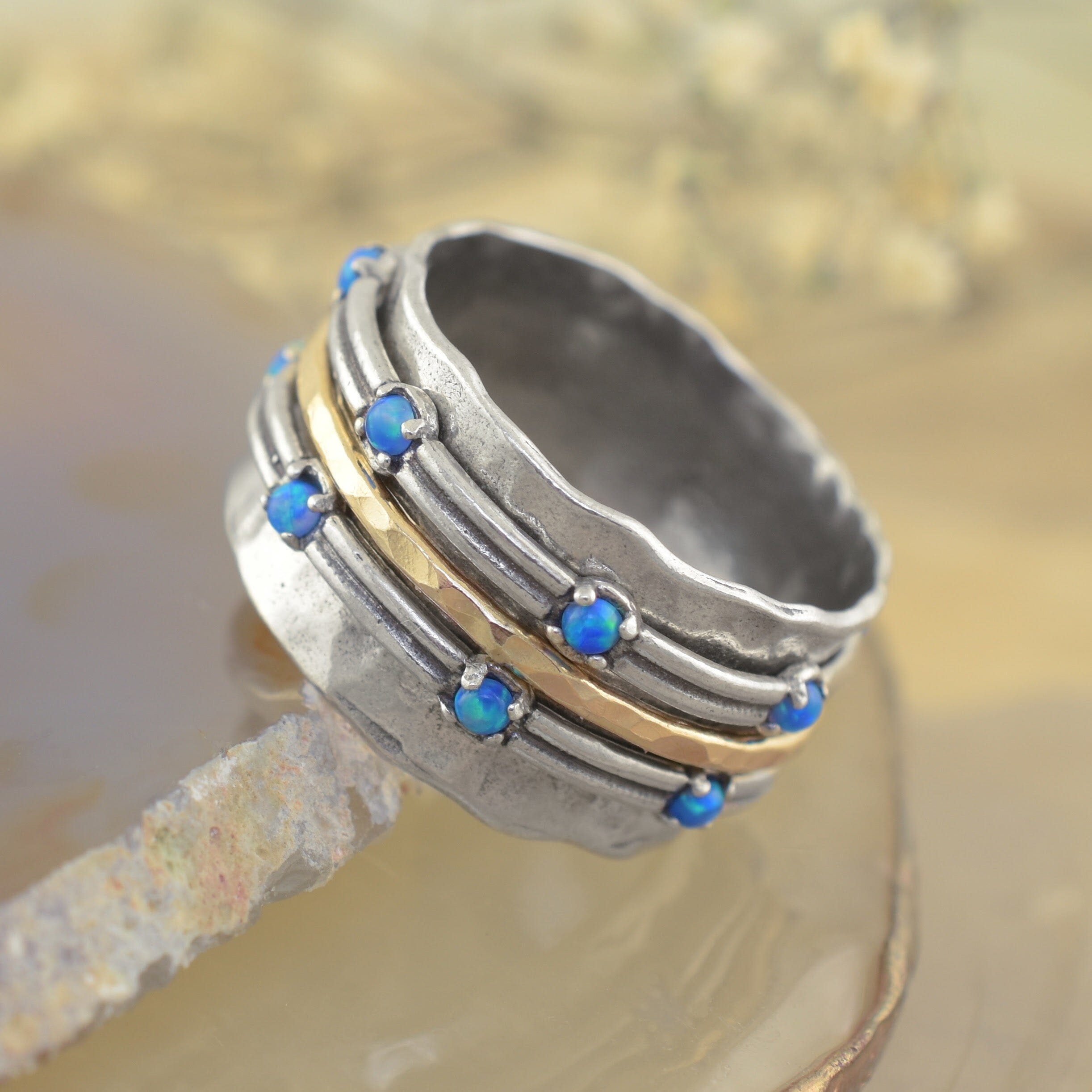 A sterling silver ring with a hammered texture, featuring small opal stones spaced across two bands with a gold band as a spacer between the two