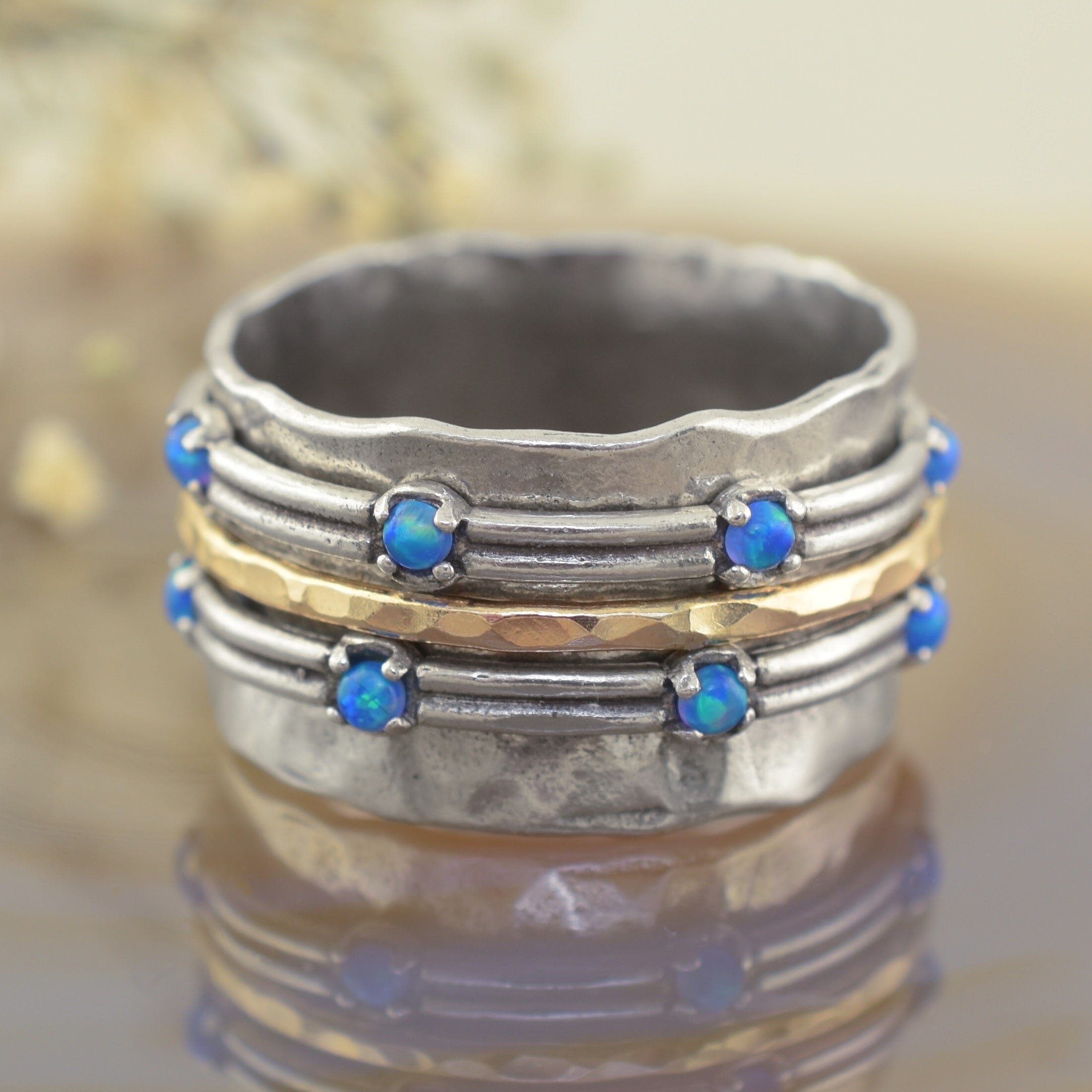 A handmade sterling silver ring with a wavy, layered design, featuring rows of small blue opal gemstones and a central hammered gold band