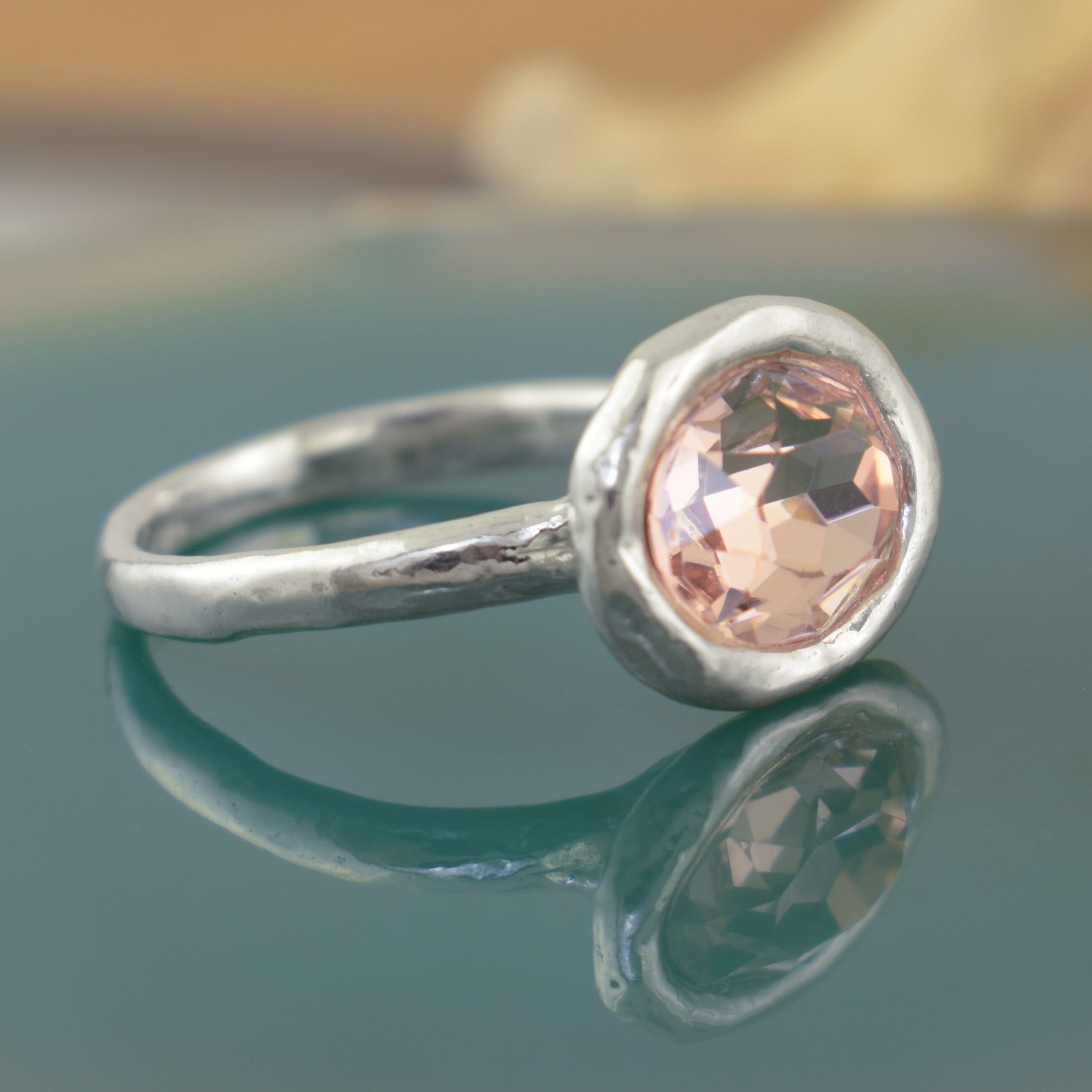 a sterling silver ring with a large, oval, faceted peach gemstone sitting on a handcrafted hammered band