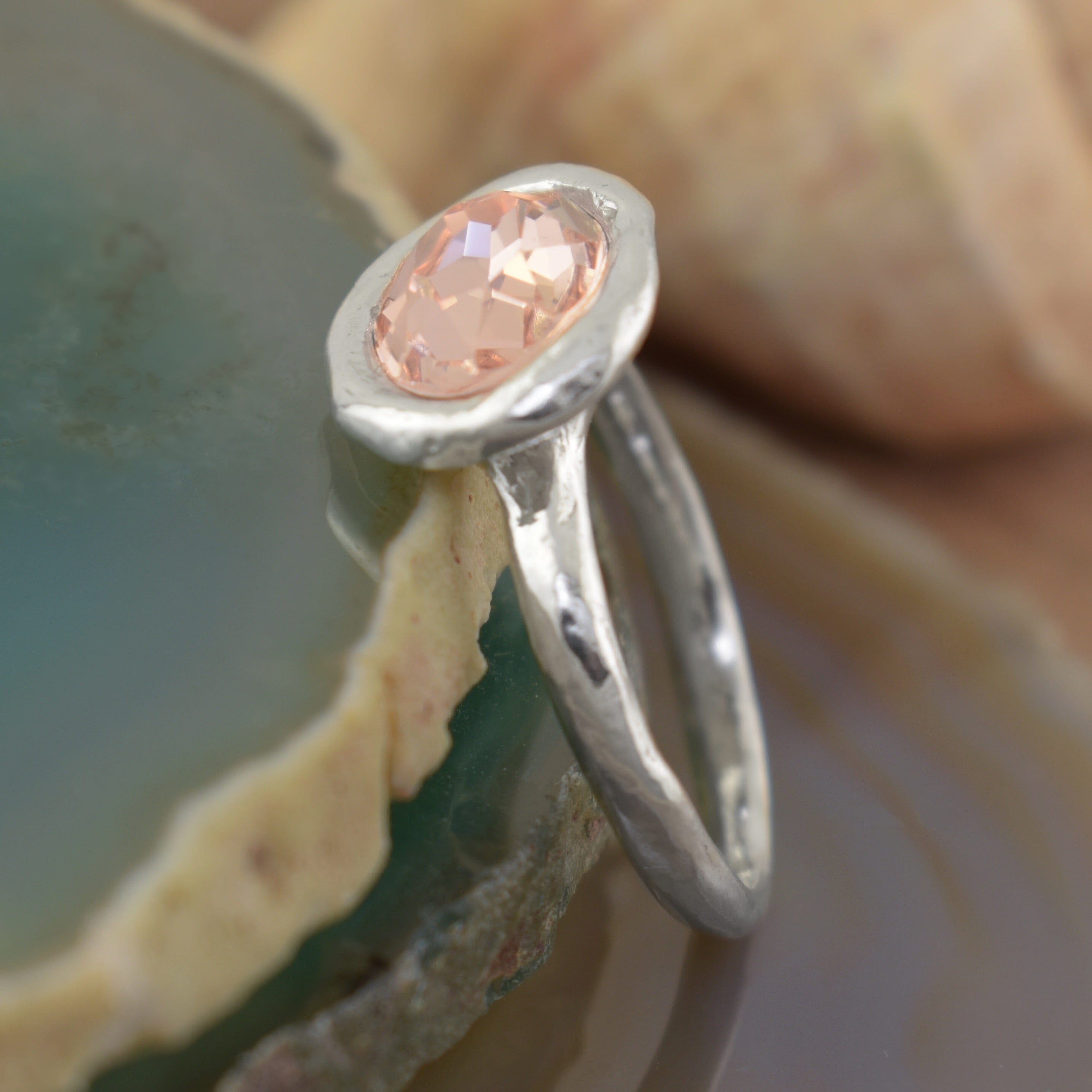 a sterling silver ring with a faceted peach oval gemstone sitting on a handcrafted hammered band