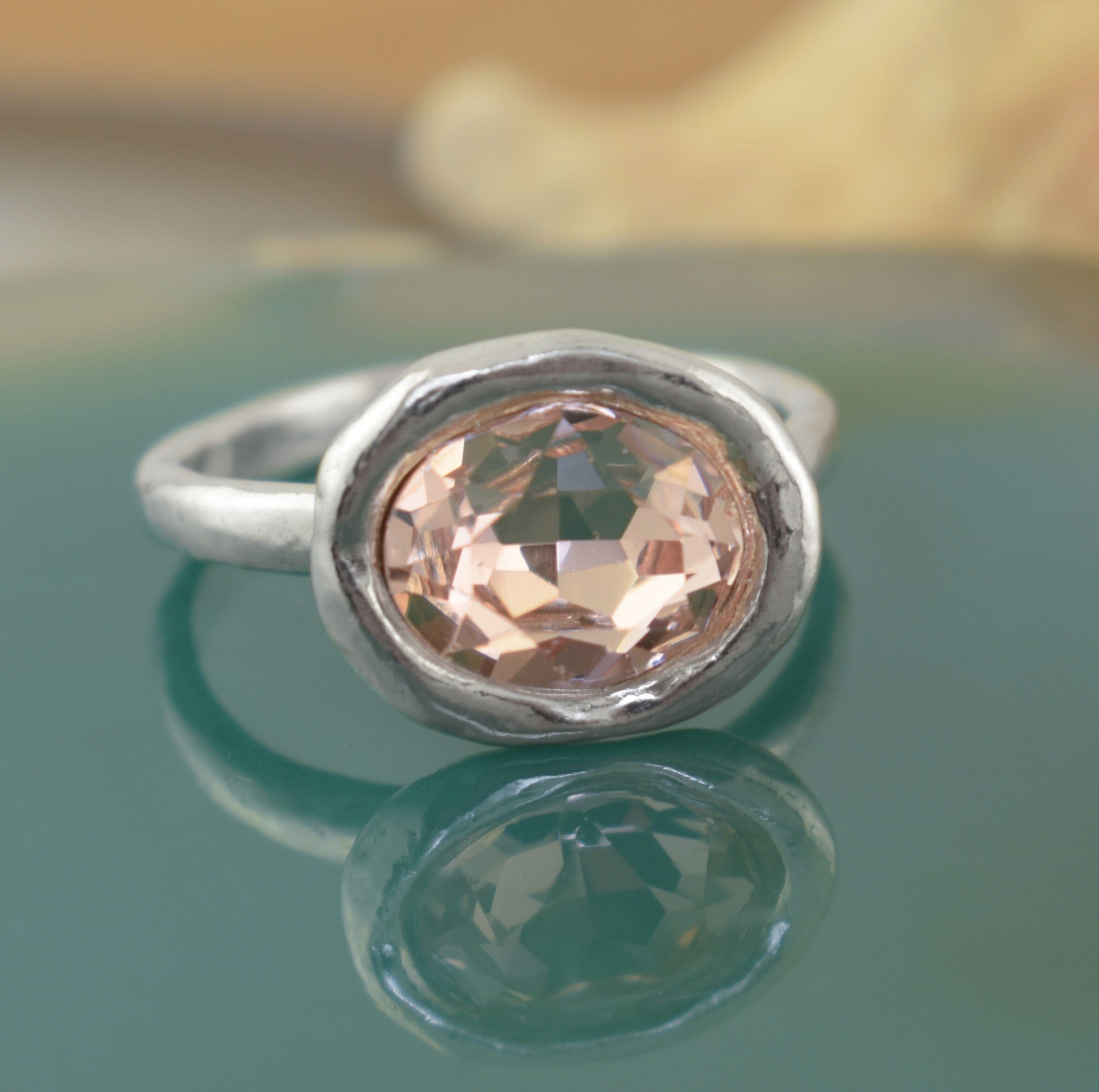 a sterling silver ring with a large, oval-cut peach faceted gemstone, sitting on a handcrafted hammered band
