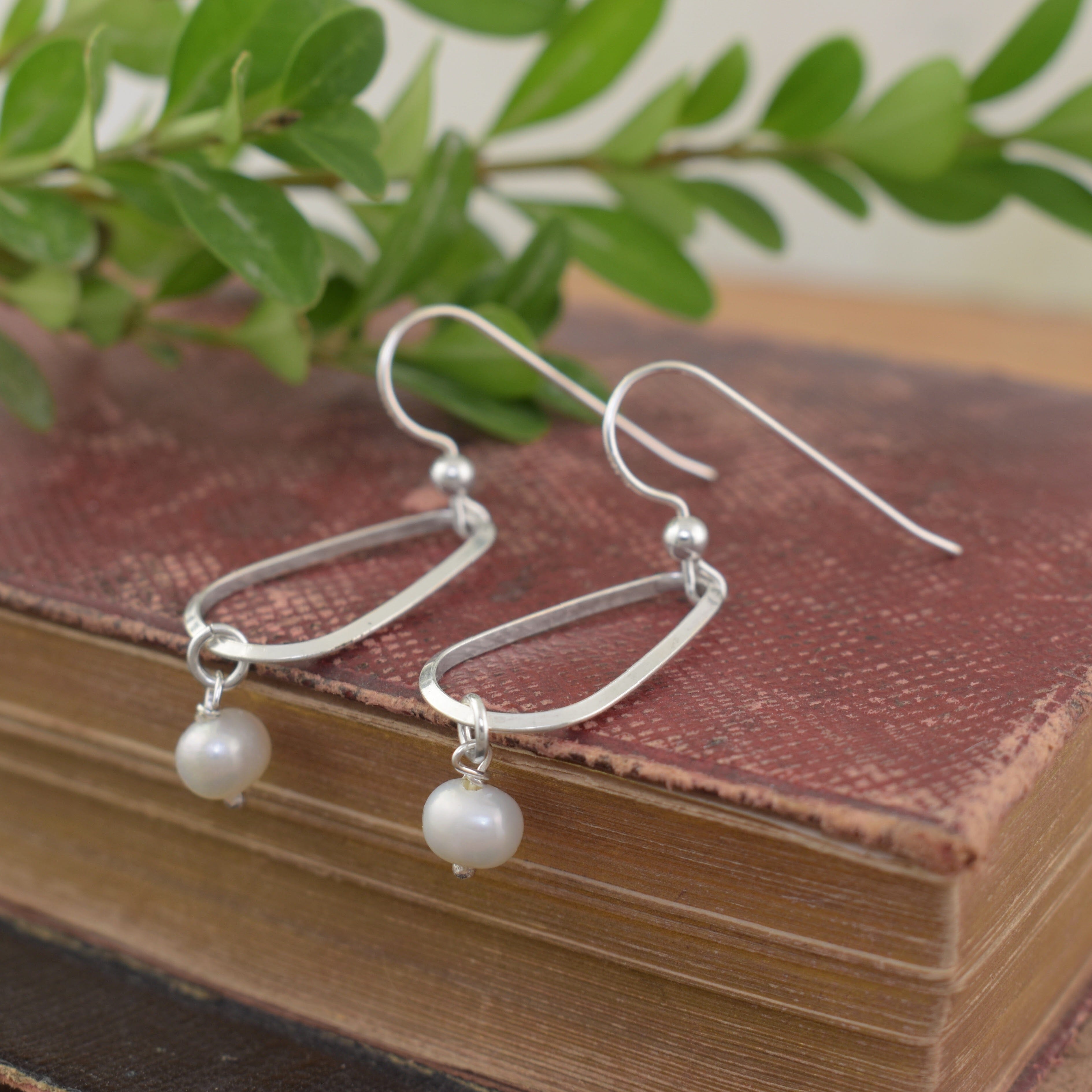 A pair of sterling silver dangle earrings with open oval hoops and small white pearl drops