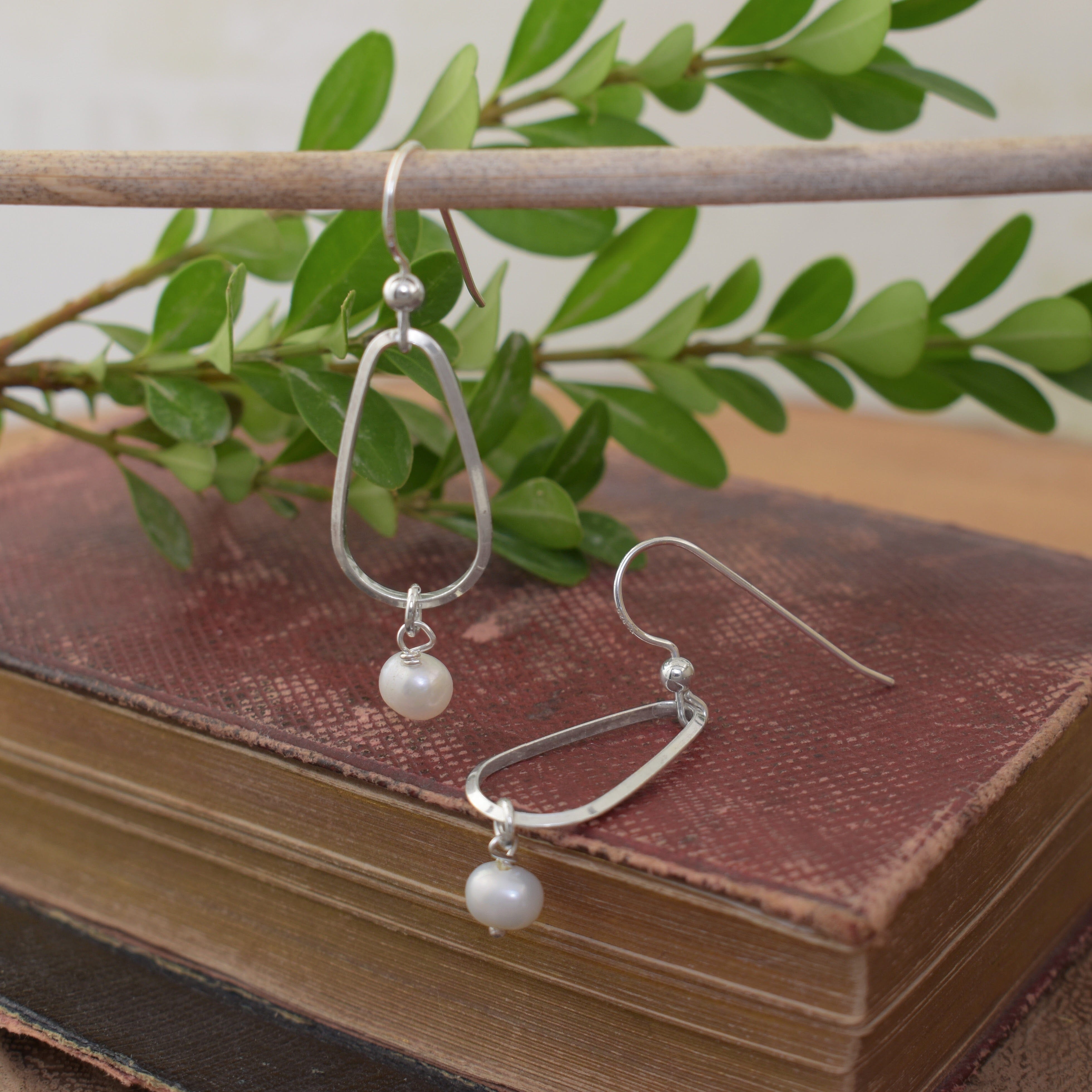 A pair of sterling silver dangle earrings with open oval hoops and small white pearl drops