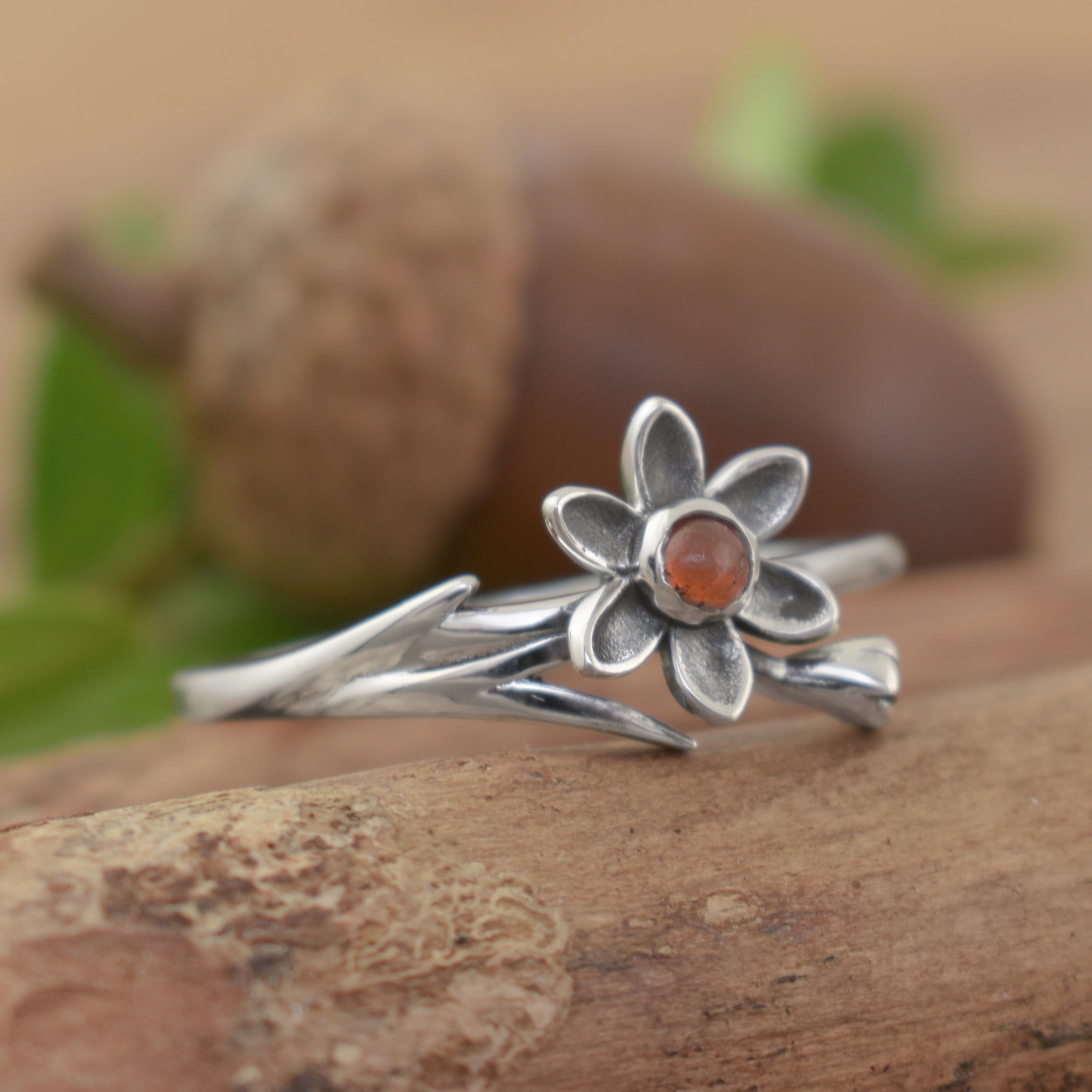 A sterling silver ring with an orange stone in the center of a flower and a flower stem flowing along the band