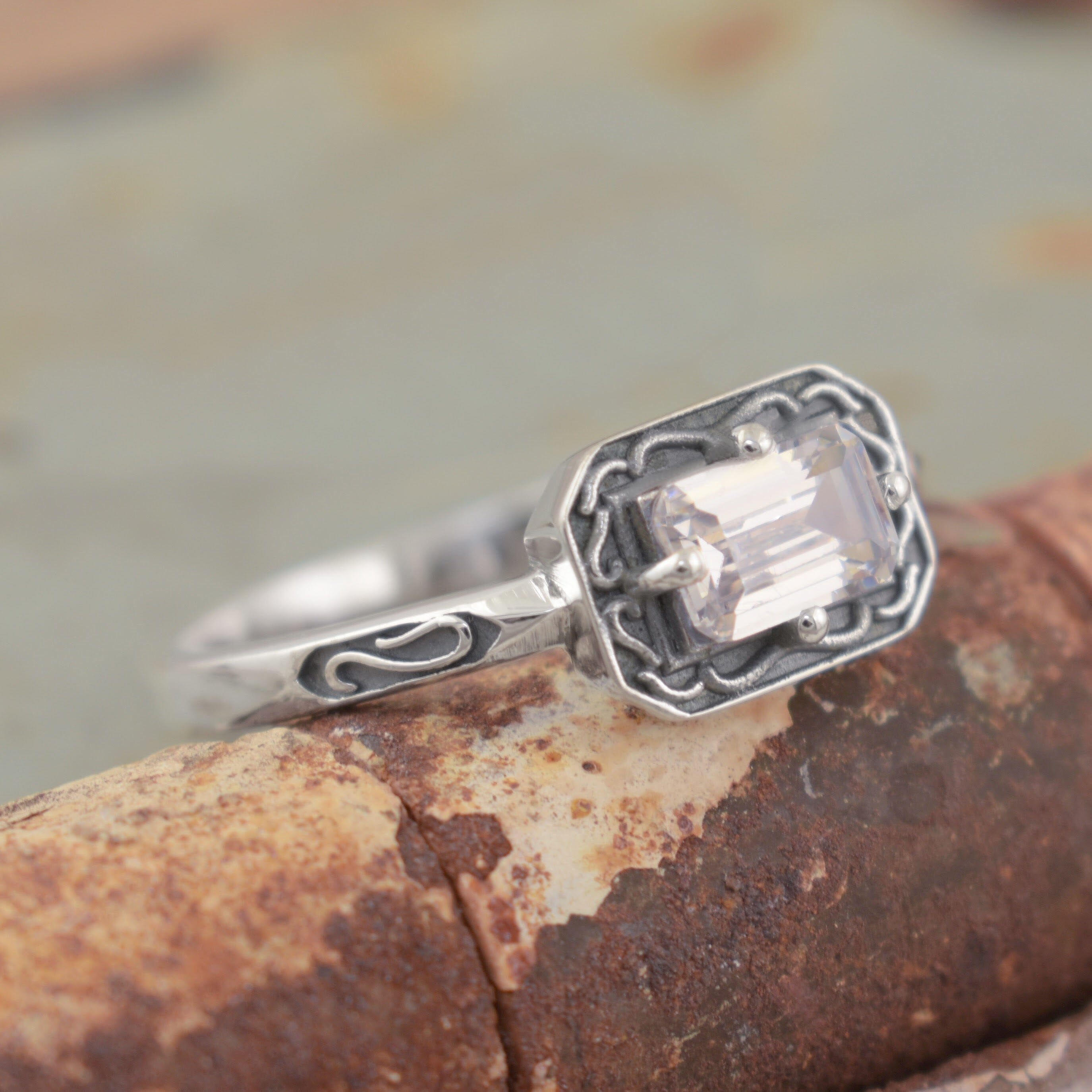 A sterling silver ring with a rectangular clear gemstone and ornate engraved detailing
