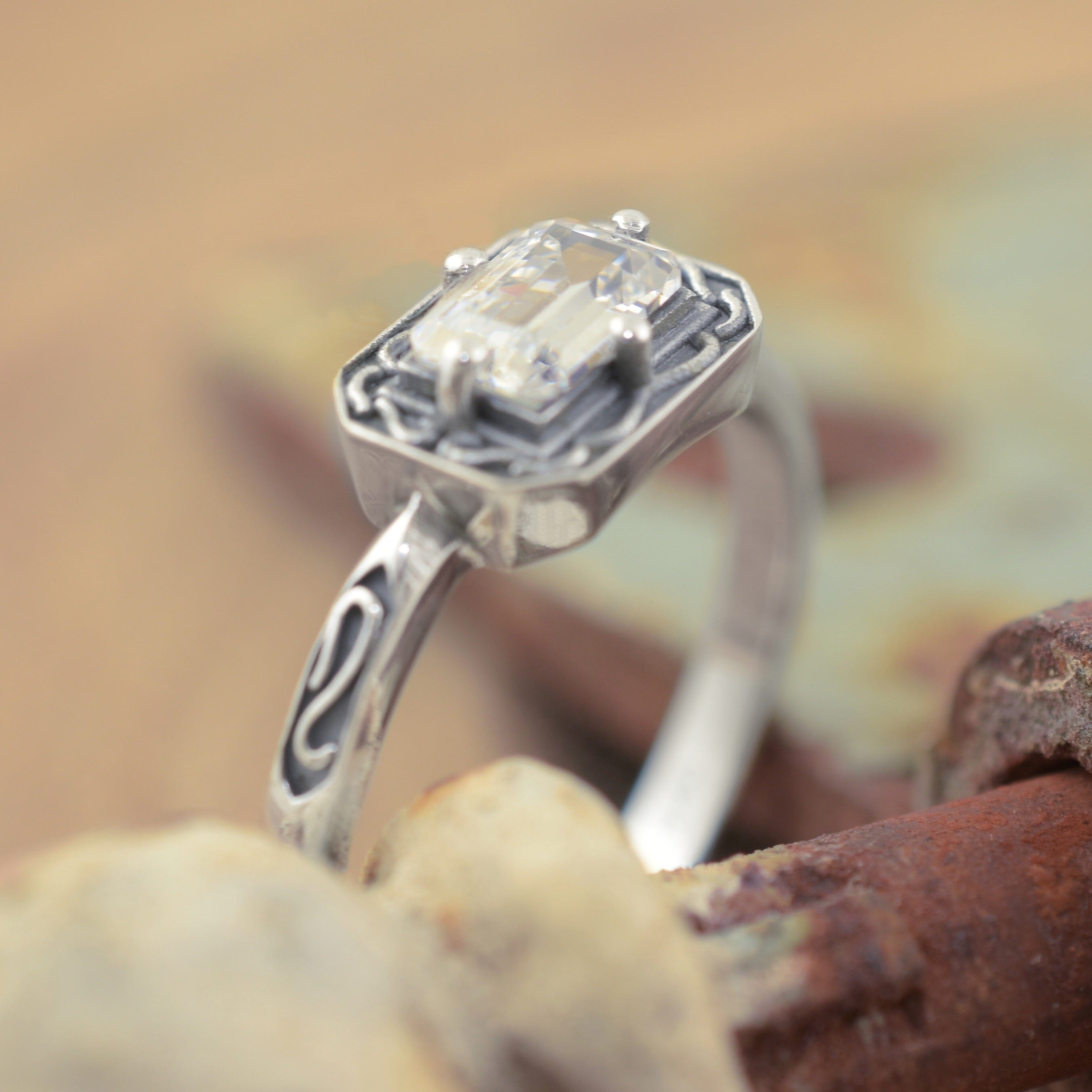 A sterling silver ring with a rectangular clear gemstone and ornate engraved detailing along the band and framing the gemstone