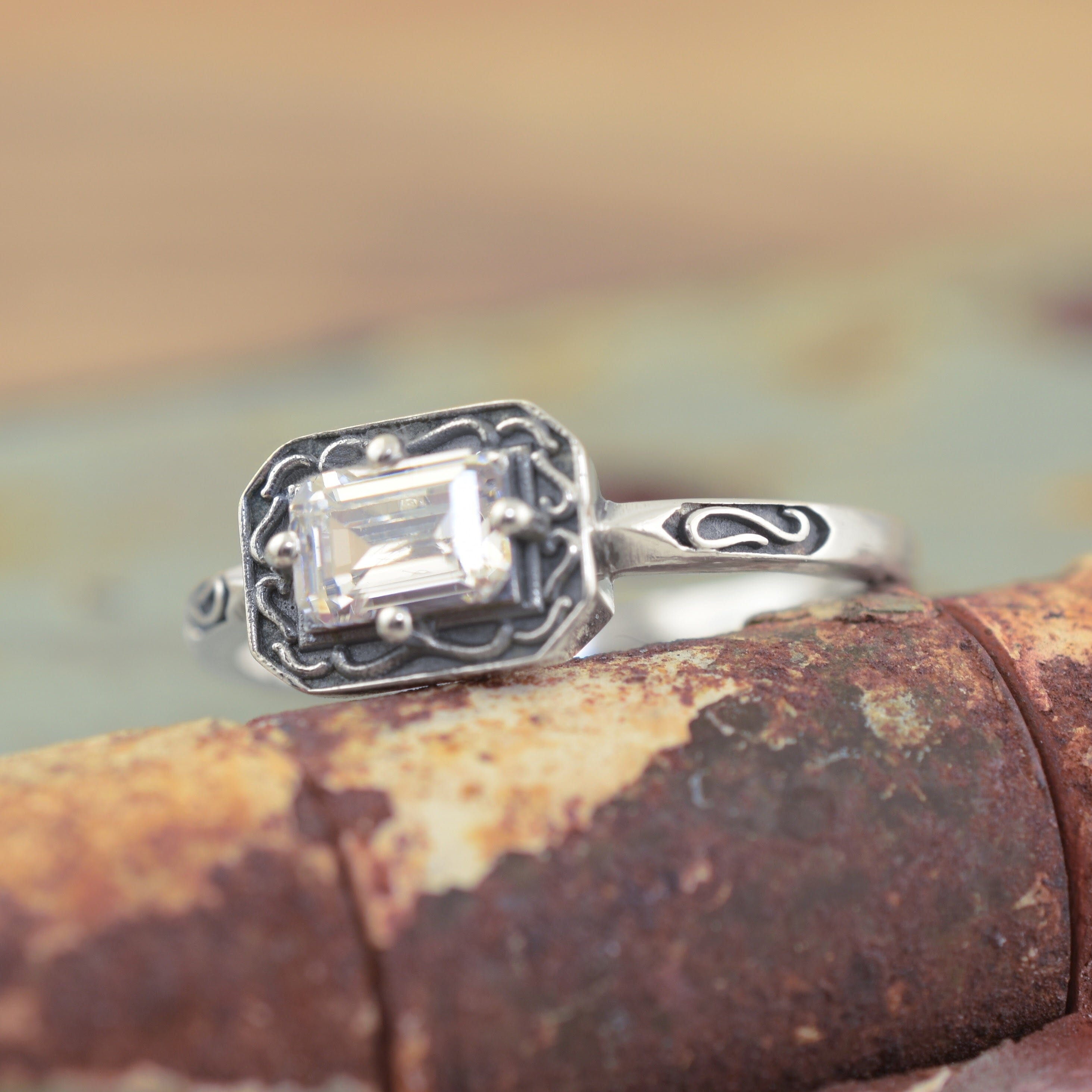 A sterling silver ring with a rectangular clear gemstone and ornate engraved detailing along the band and framing the gemstone