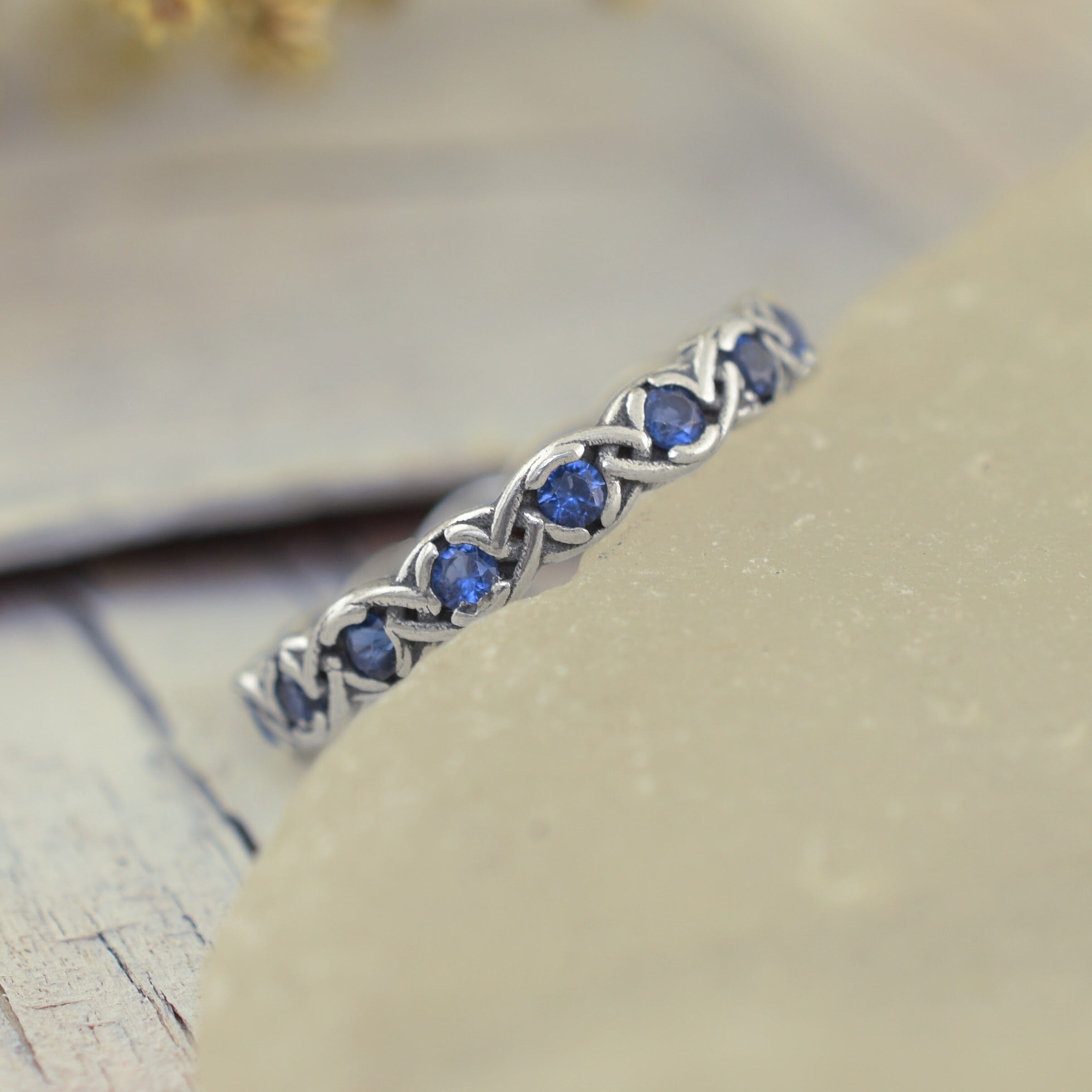 A sterling silver ring featuring a braided pattern with small round blue sapphire gemstones