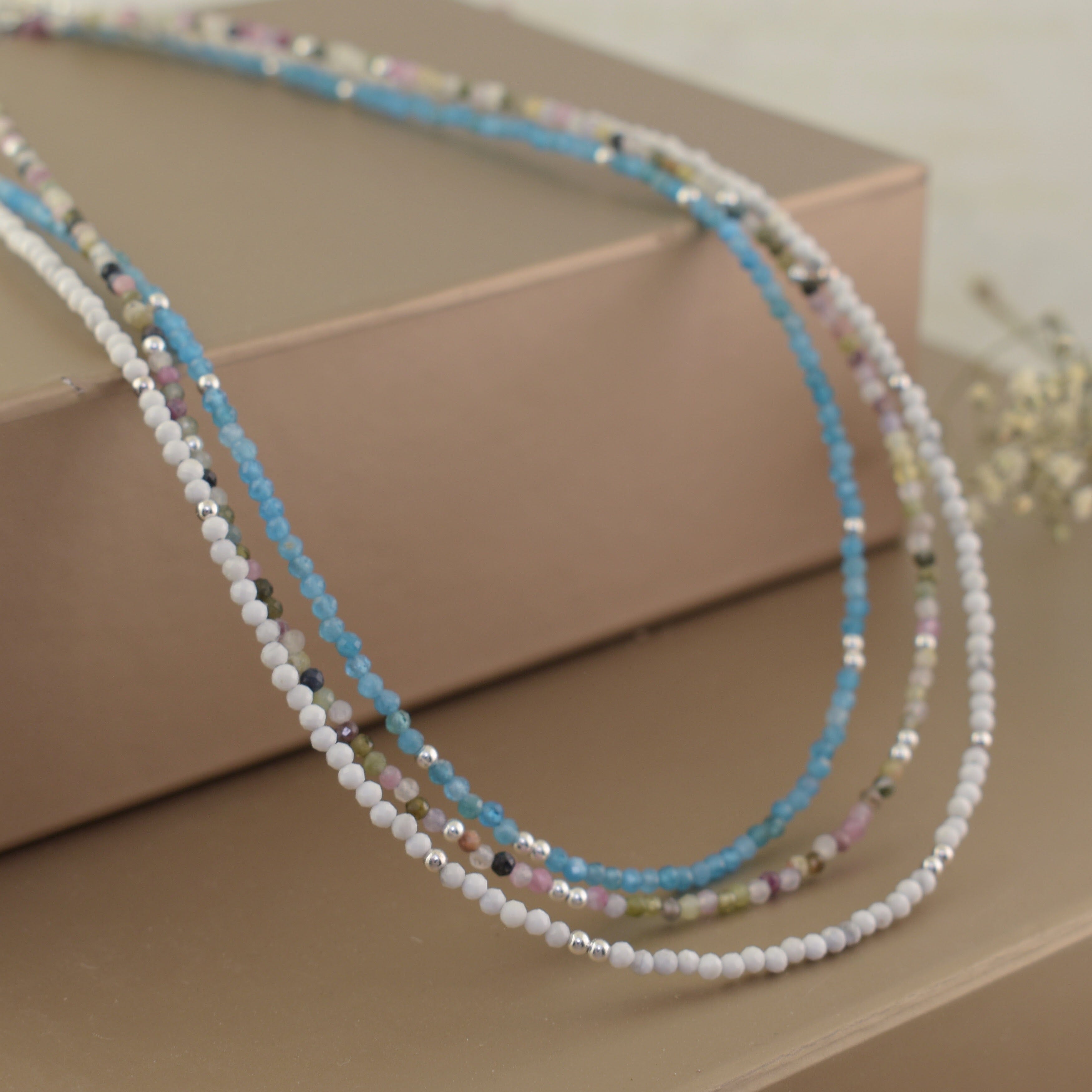 three beaded necklaces, featuring white rock crystal beads, light blue amazonite beads, and multi-colored tourmaline beads with small silver spacer beads