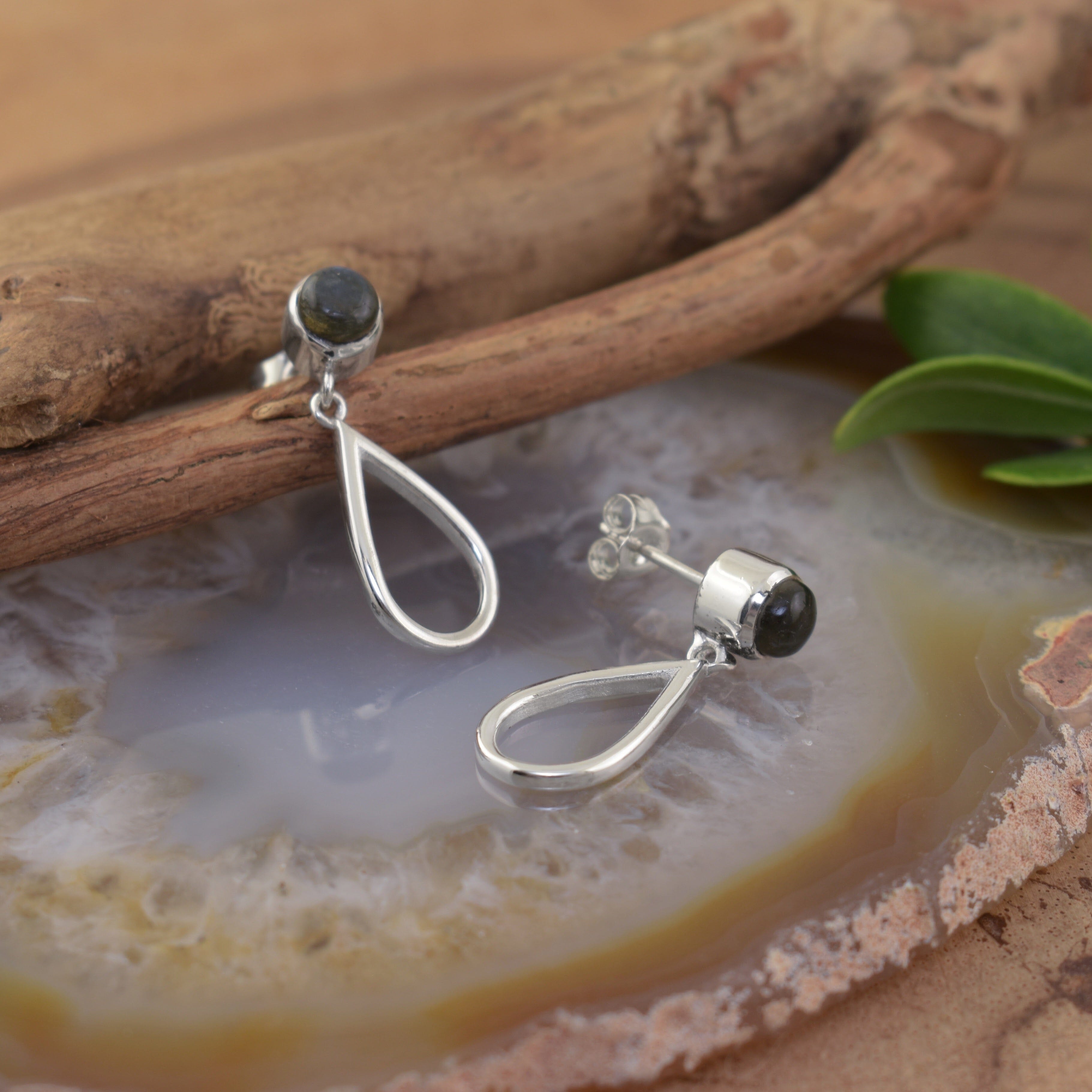A pair of sterling silver post earrings featuring labradorite stones and a silver teardrop with cutouts hanging beneath