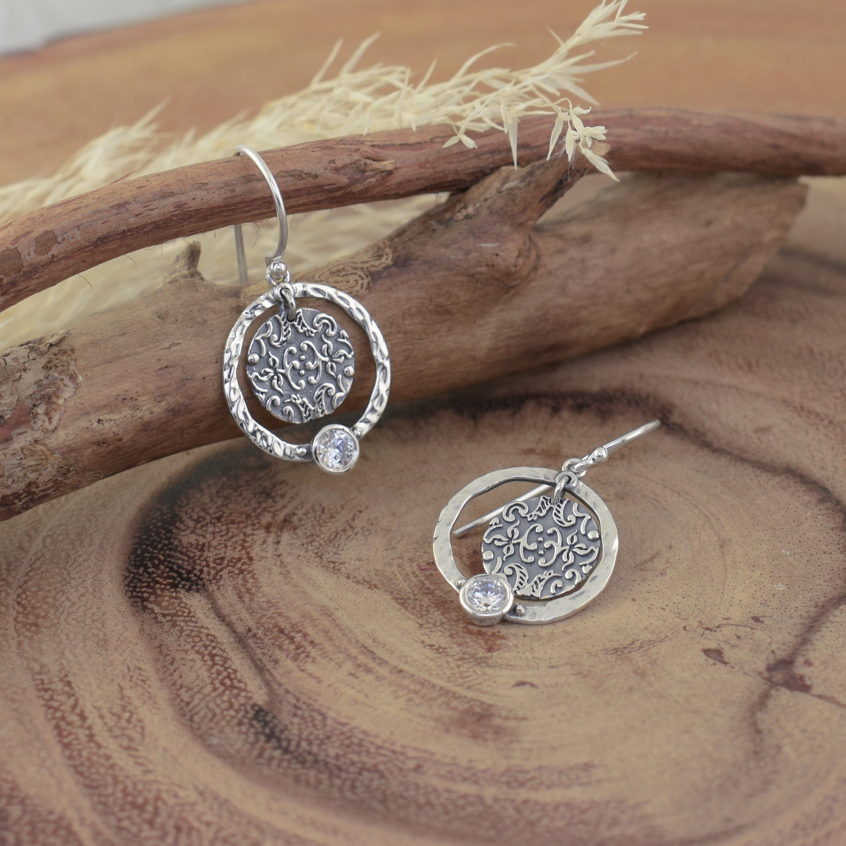 A pair of sterling silver dangle earrings featuring a round hammered hoop with an intricately details disc in the center with a small CZ stone at the bottom