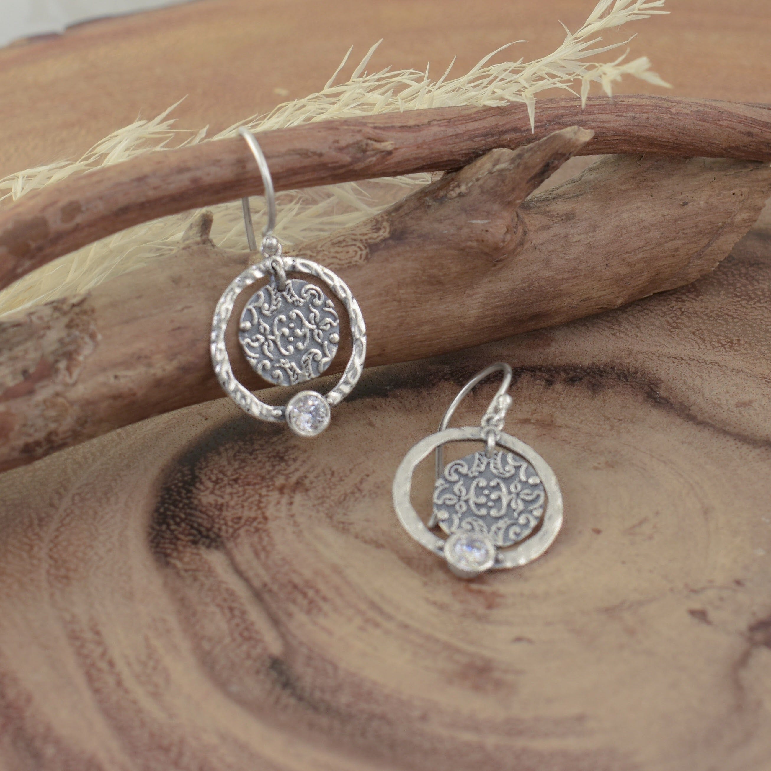 A pair of dangle sterling silver earrings with a hammered ring and engraved disc hanging in the center with a small CZ stone on the bottom