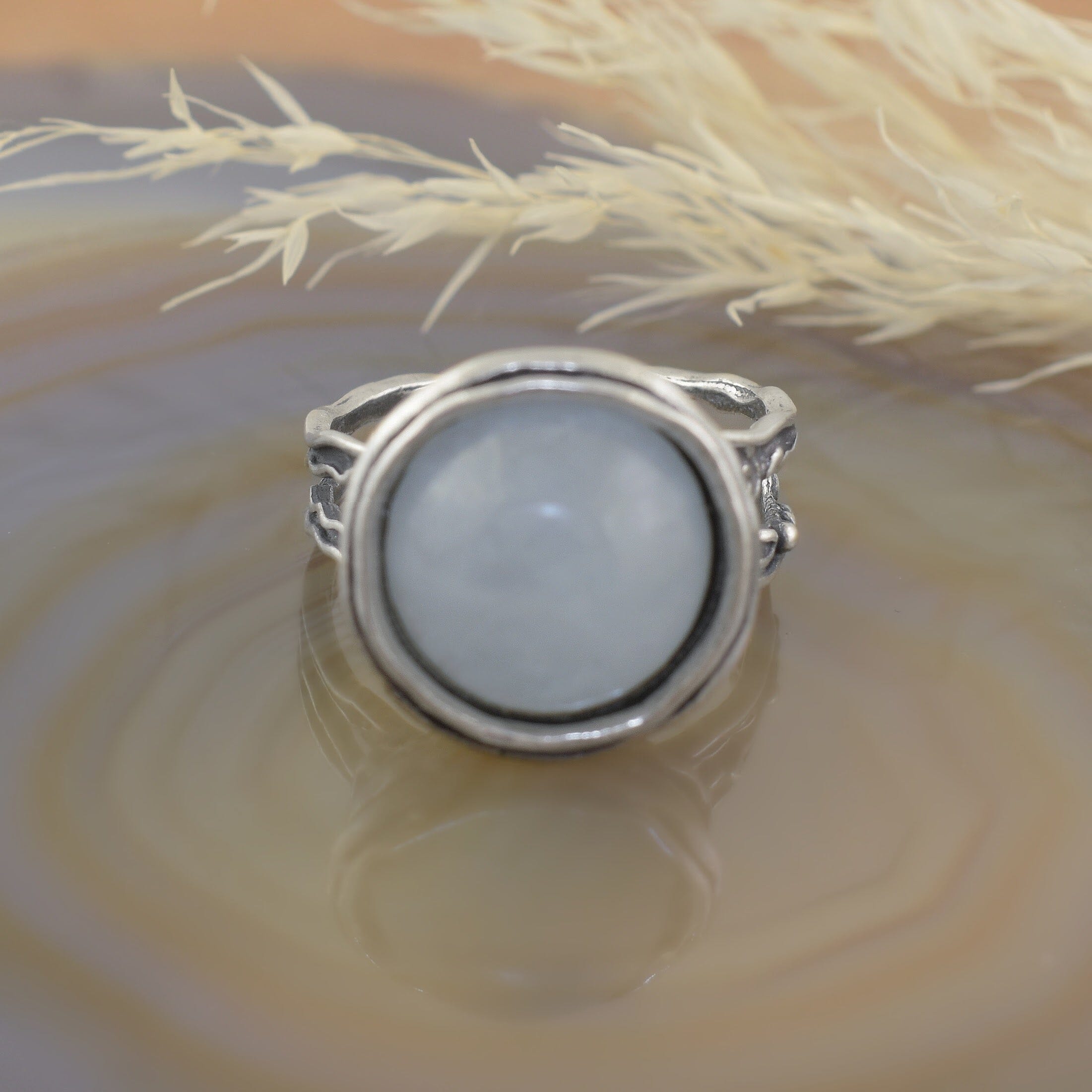 A sterling silver ring with a detailed filigree band, featuring a large round milky aquamarine stone