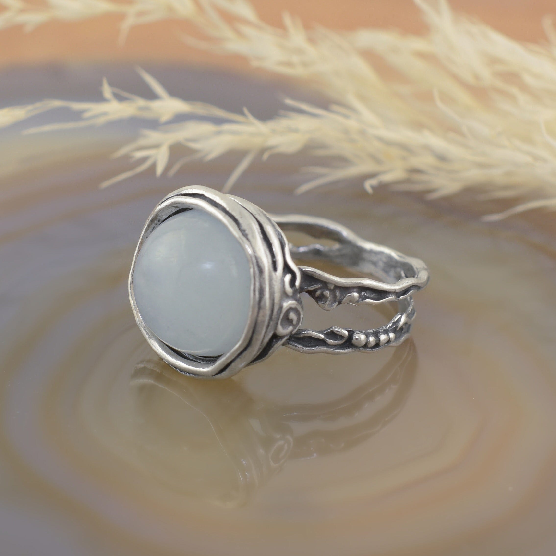 A sterling silver ring with a detailed filigree band, featuring a large round milky aquamarine stone