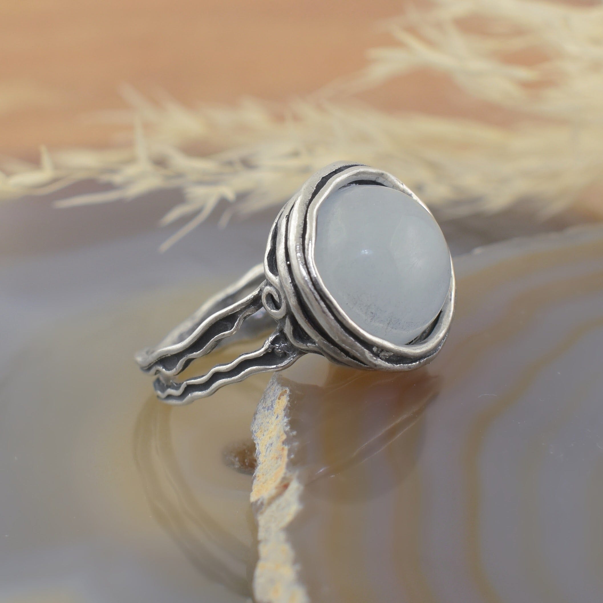 A sterling silver ring with a detailed filigree band, featuring a large round milky aquamarine stone