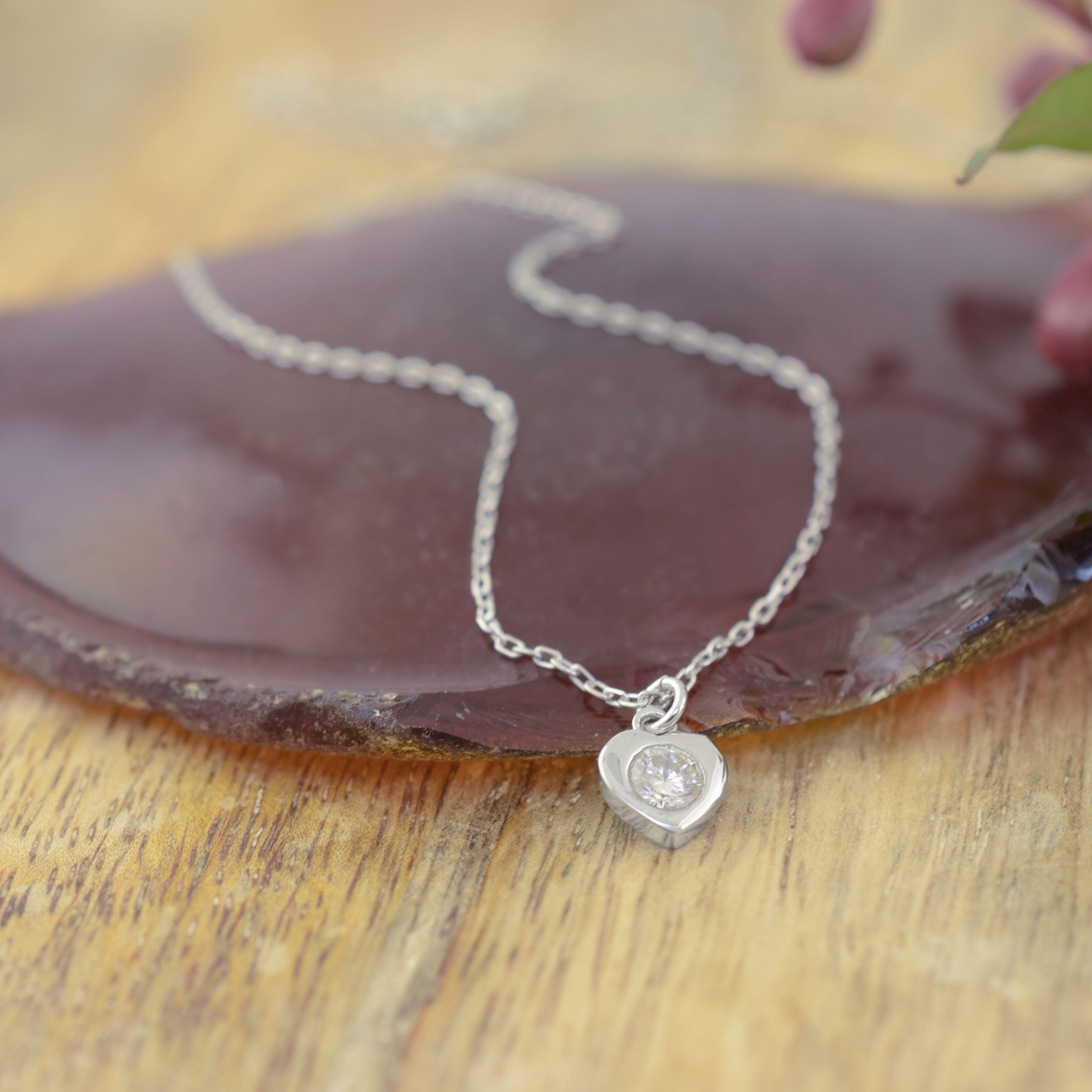 a delicate sterling silver chain necklace with a small heart-shaped pendant set with a clear gemstone