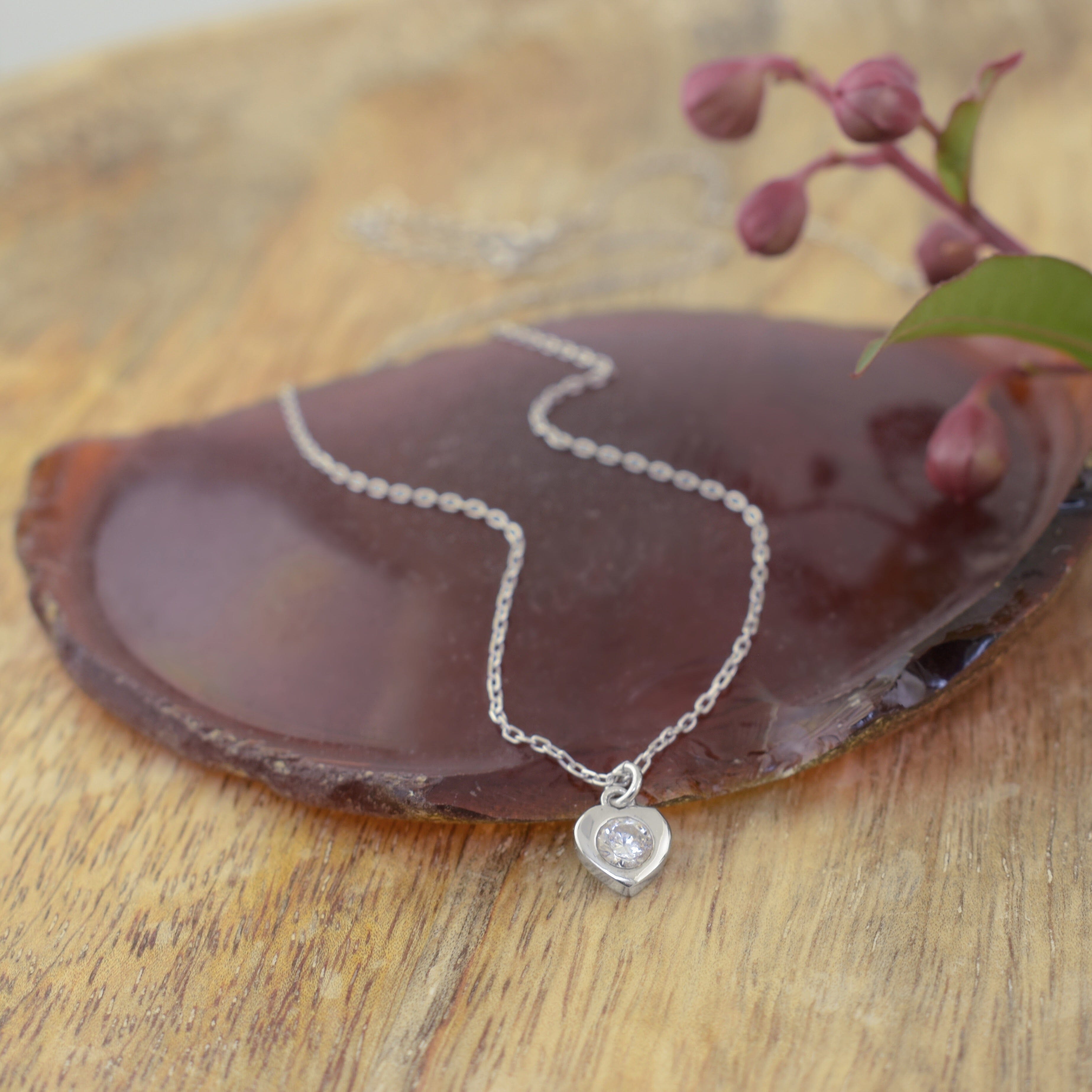 a delicate sterling silver chain necklace with a small heart-shaped pendant set with a clear gemstone