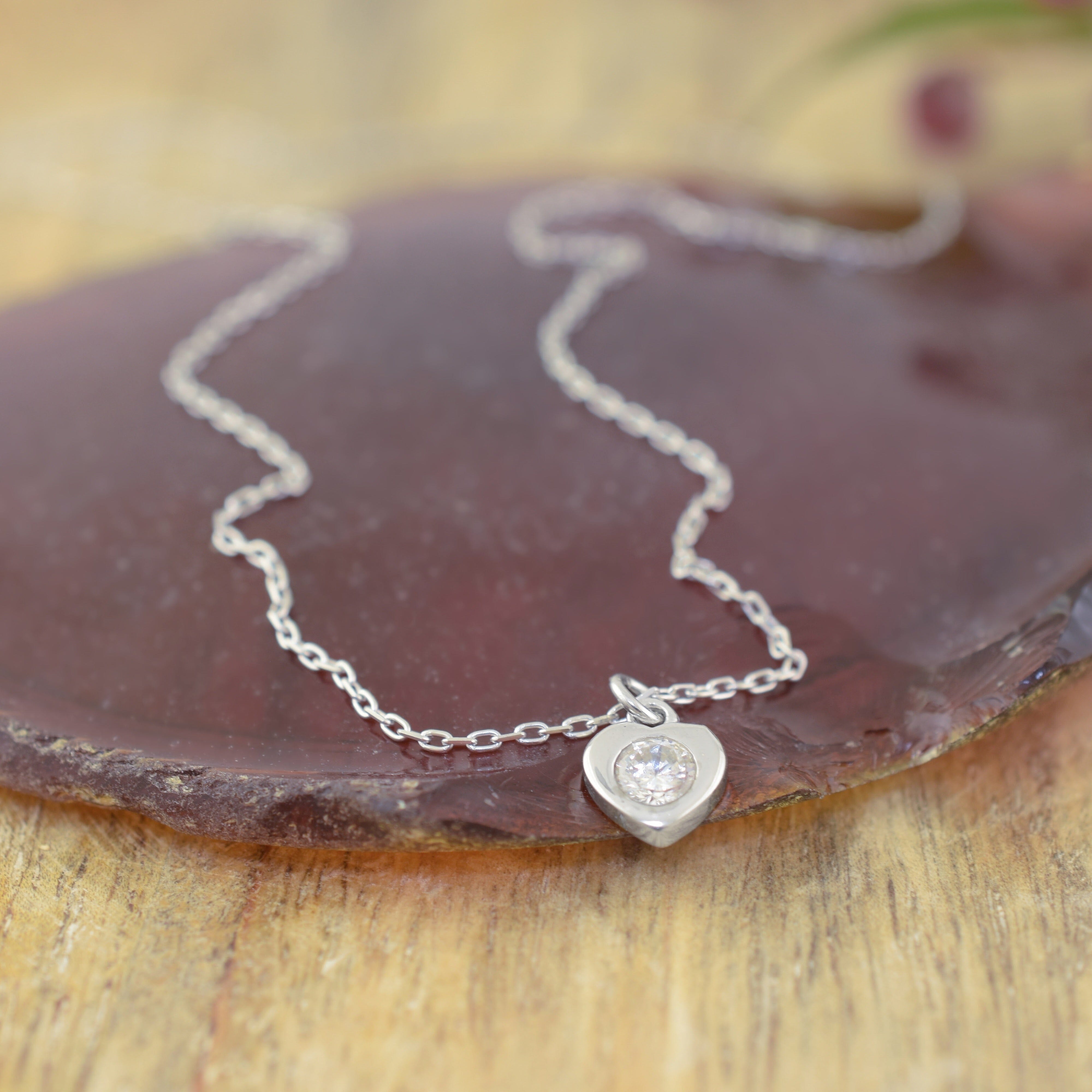 a delicate sterling silver chain necklace with a small heart-shaped pendant set with a clear gemstone