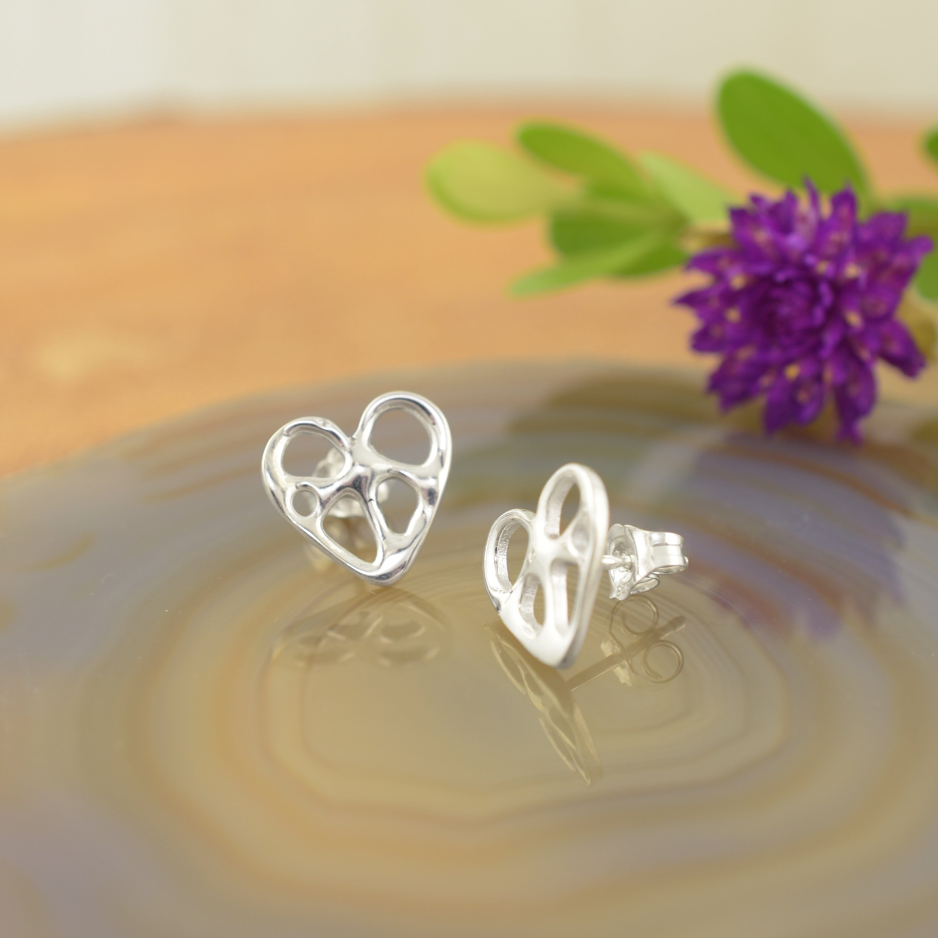 A pair of sterling silver post earrings, featuring an organic heart with little cut outs