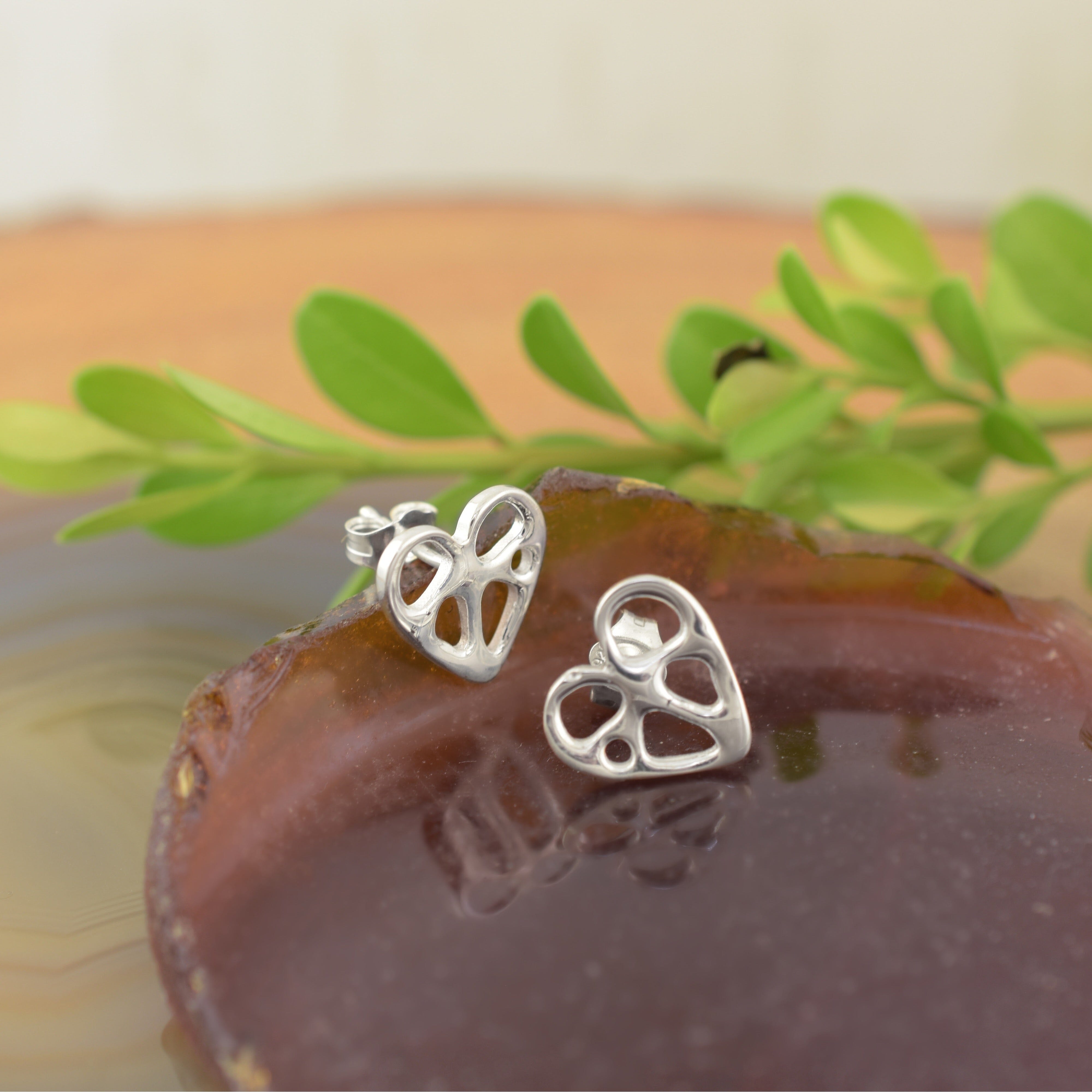 A pair of sterling silver post earrings, featuring an organic heart with little cut outs