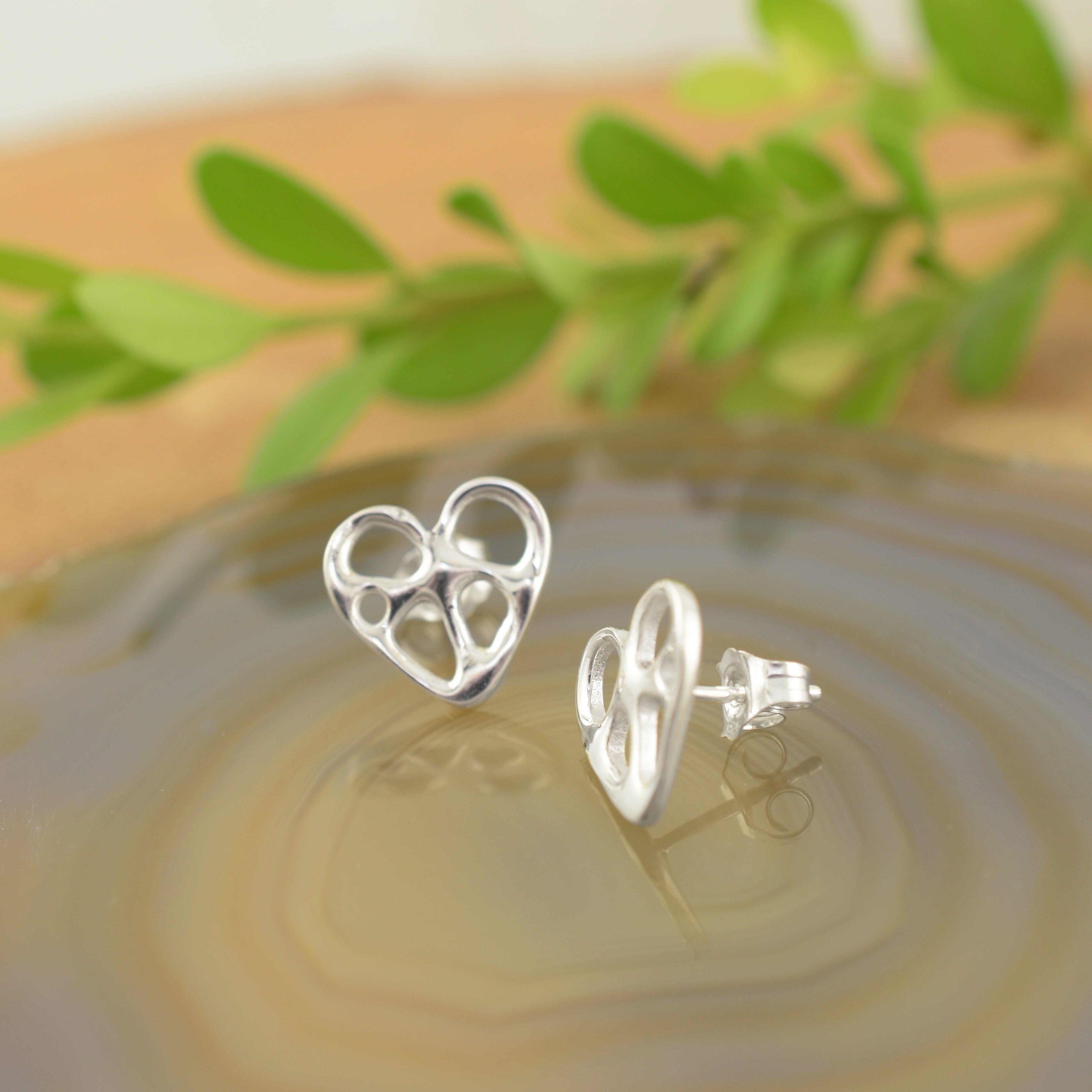 A pair of sterling silver post earrings, featuring an organic heart with little cut outs