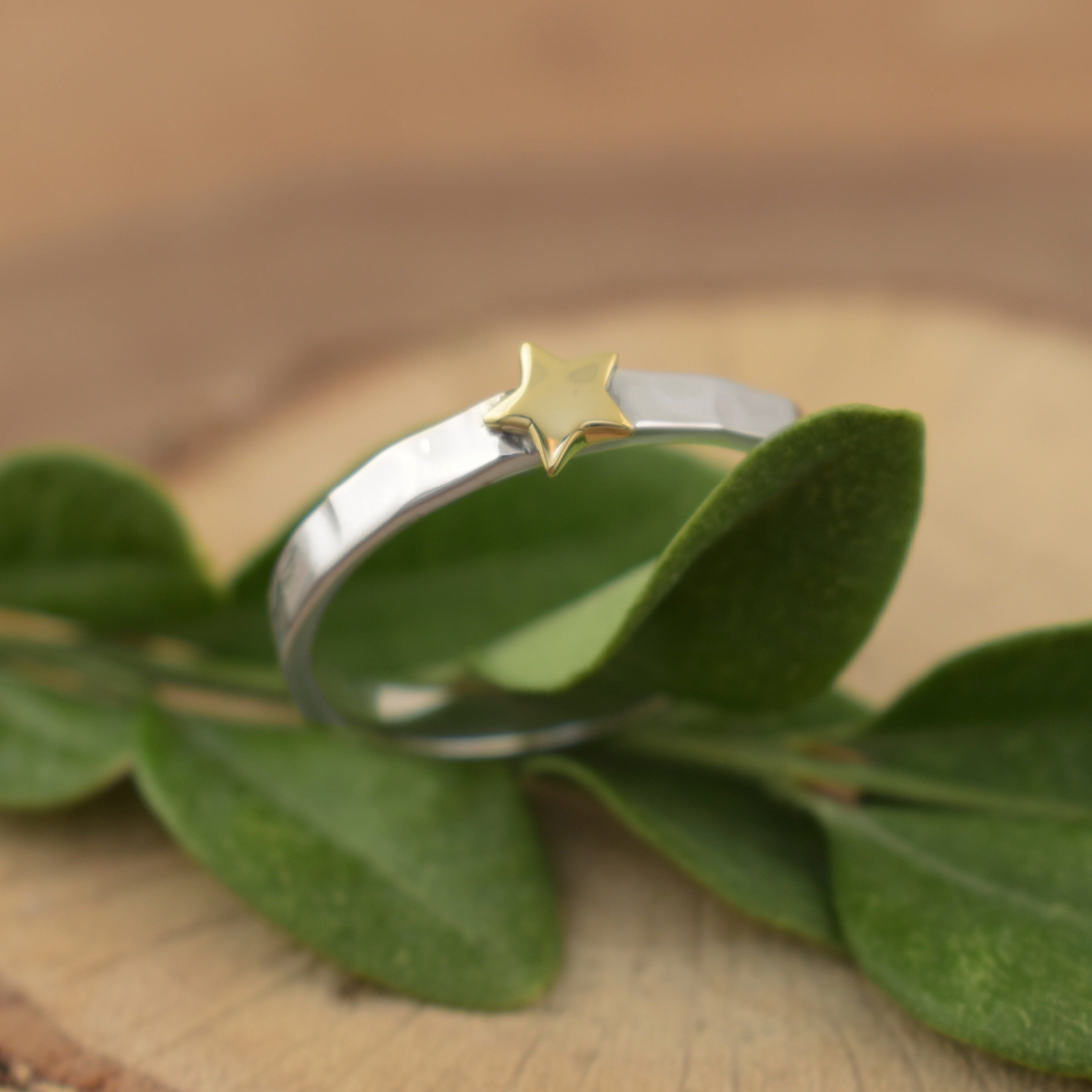 A small sterling silver ring with a hammered band texture, featuring a polished brass star in the middle of the band