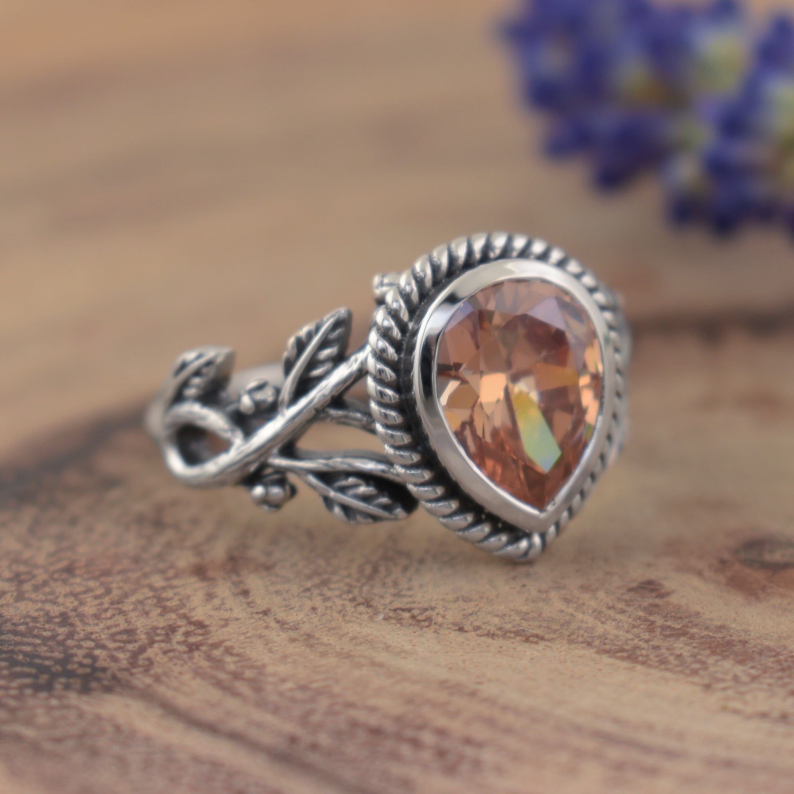 A sterling silver ring featuring a teardrop-shaped sunset orange stone and vine-like details along the band