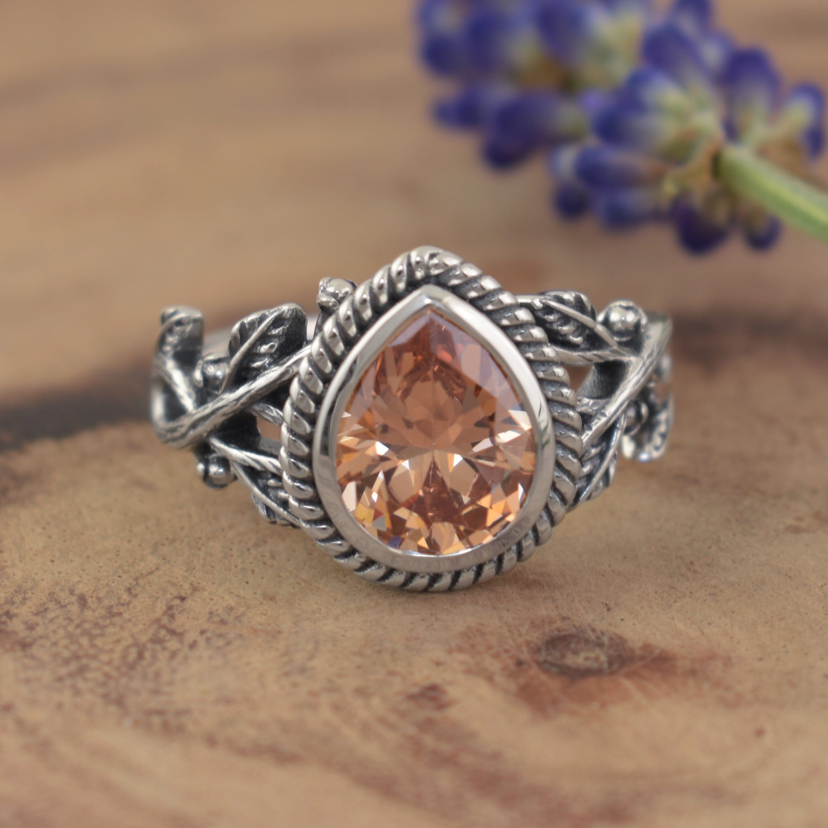 A sterling silver ring featuring a large teardrop-shaped sunset orange stone and intricate vine details along the band