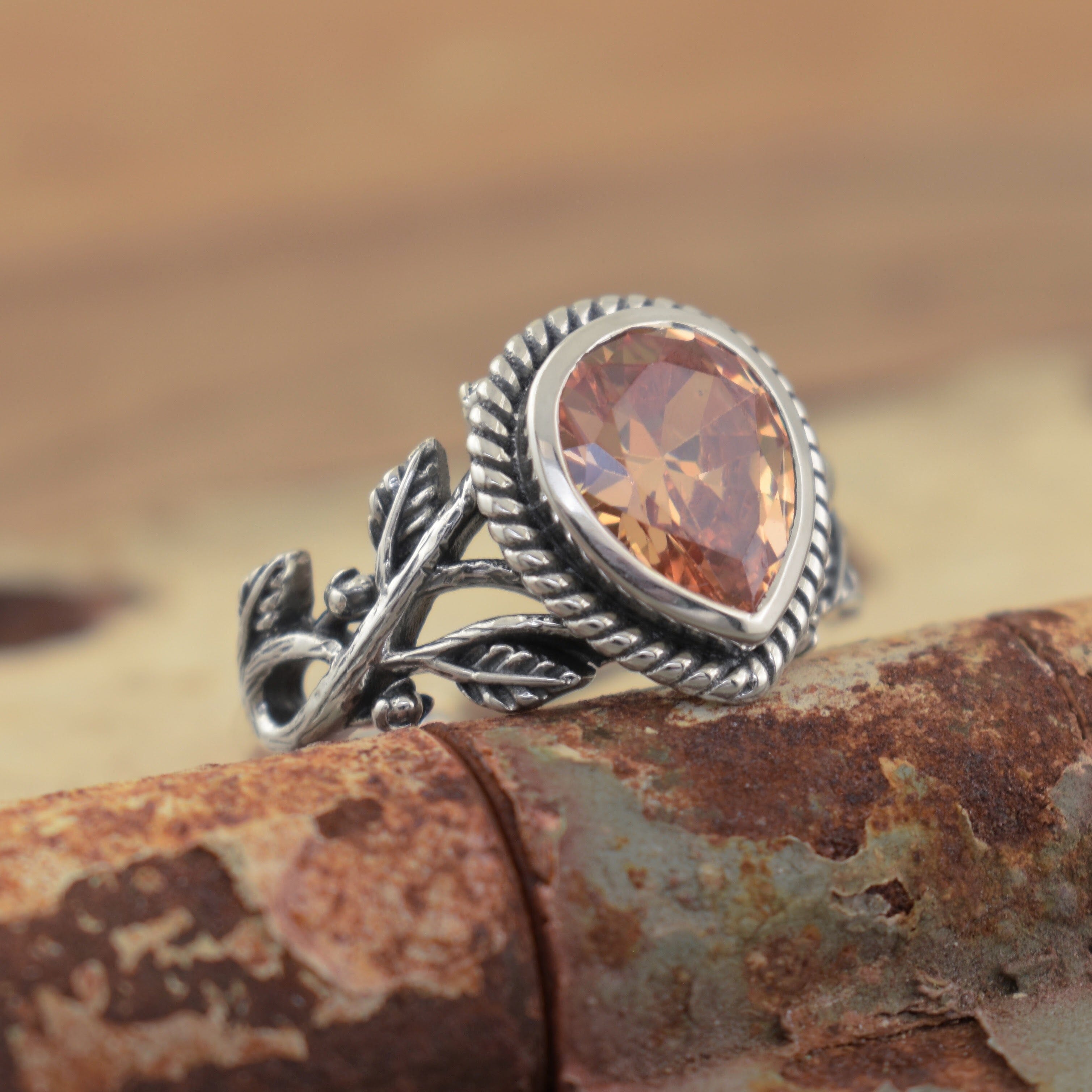 A sterling silver ring featuring a sunset orange teardrop-shaped stone framed by a rope pattern and intricate vine details along the band