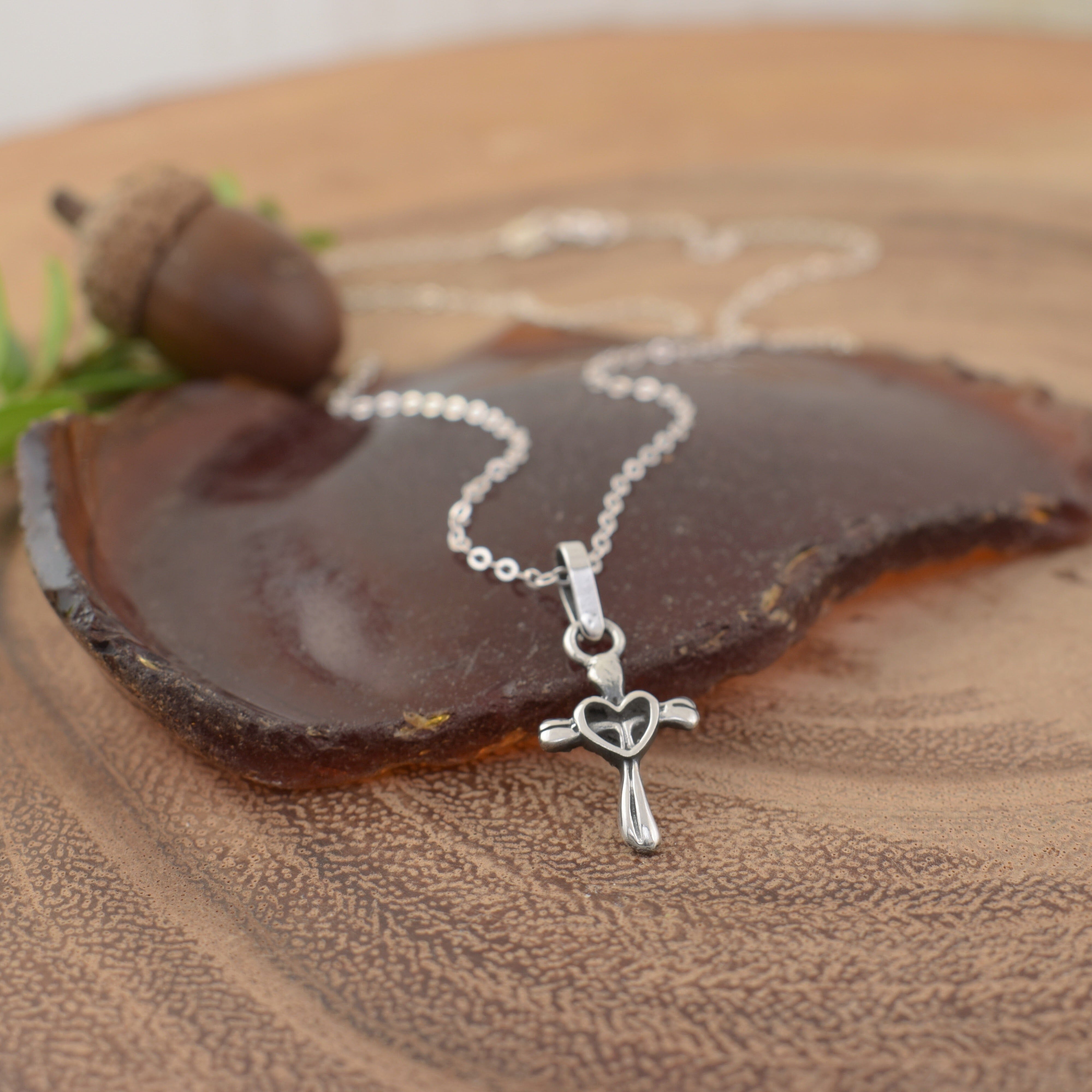 A sterling silver necklace with a dangling cross pendant with a heart outline in the center
