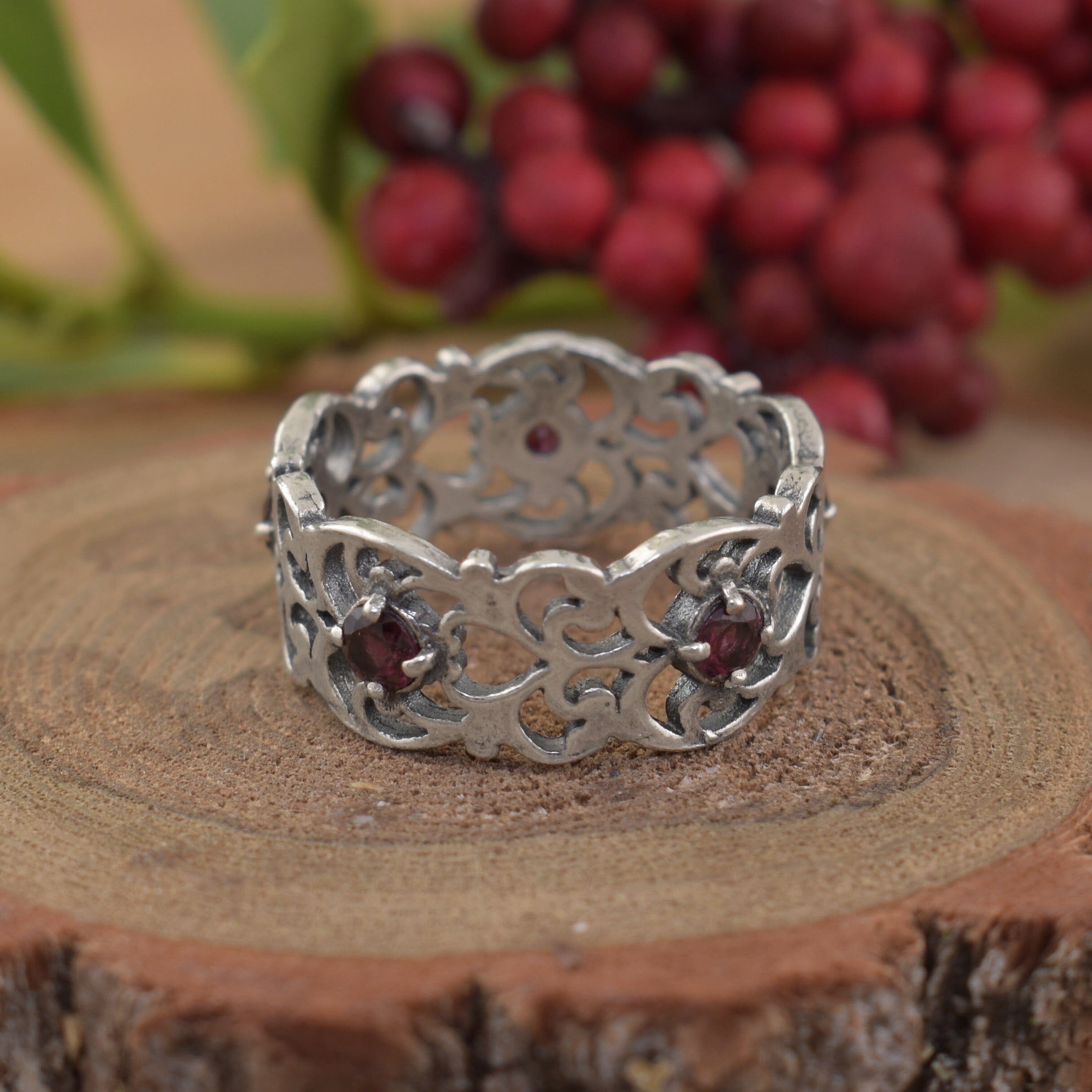 A sterling silver filigree band featuring small round garnet stones spaced along the center of the band