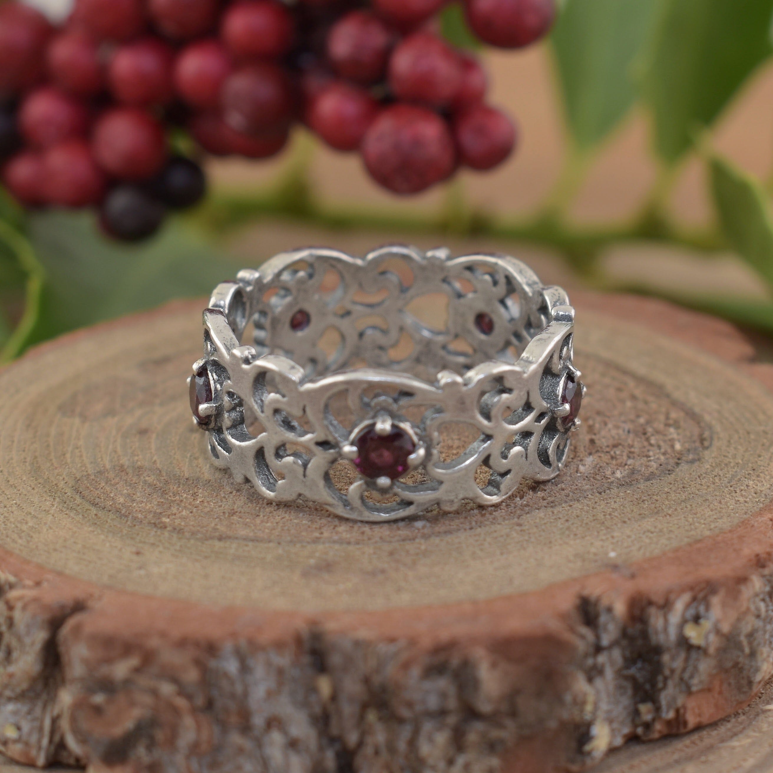 A sterling silver filigree band featuring small round garnet stones spaced along the center of the band