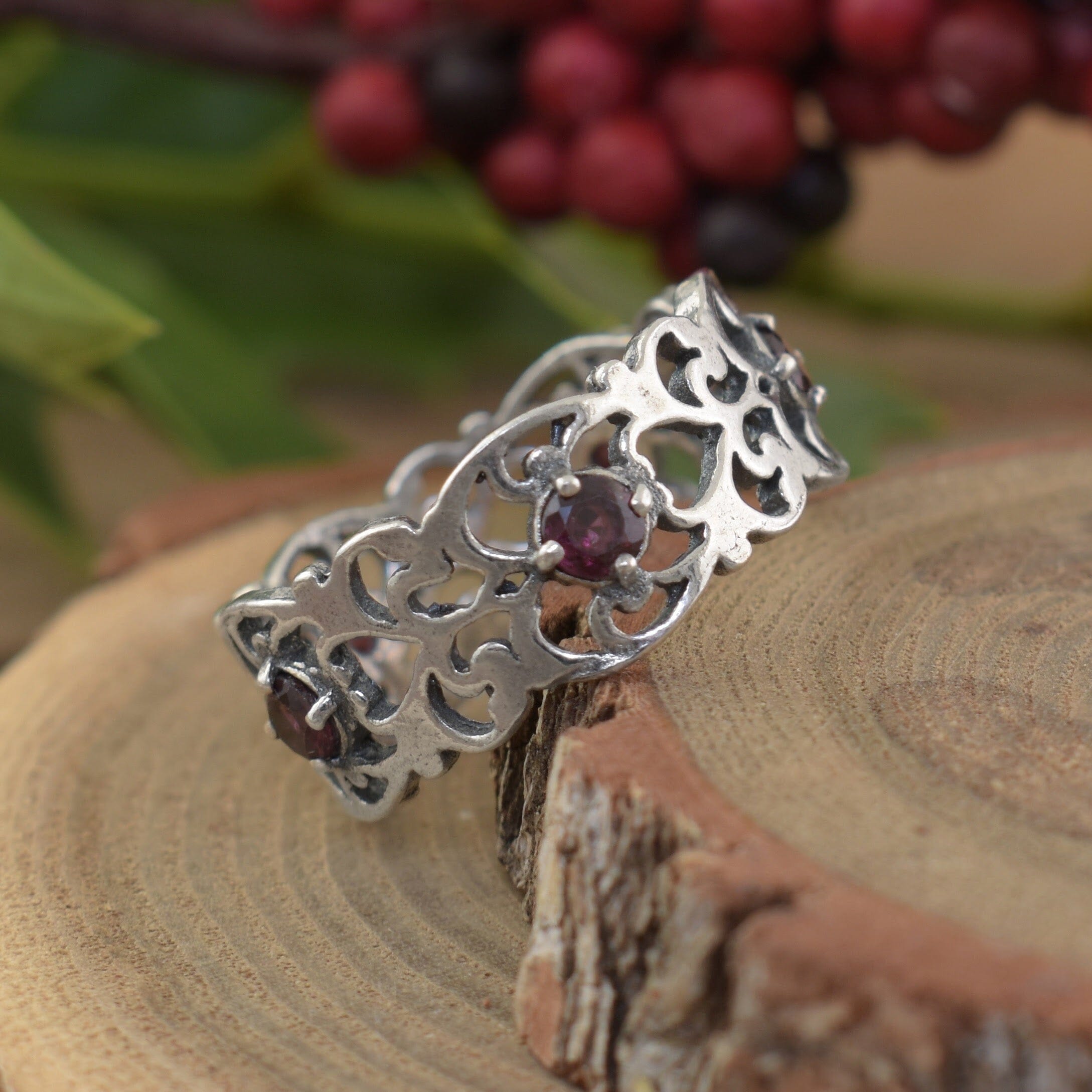 A sterling silver filigree band featuring small round garnet stones spaced along the center of the band