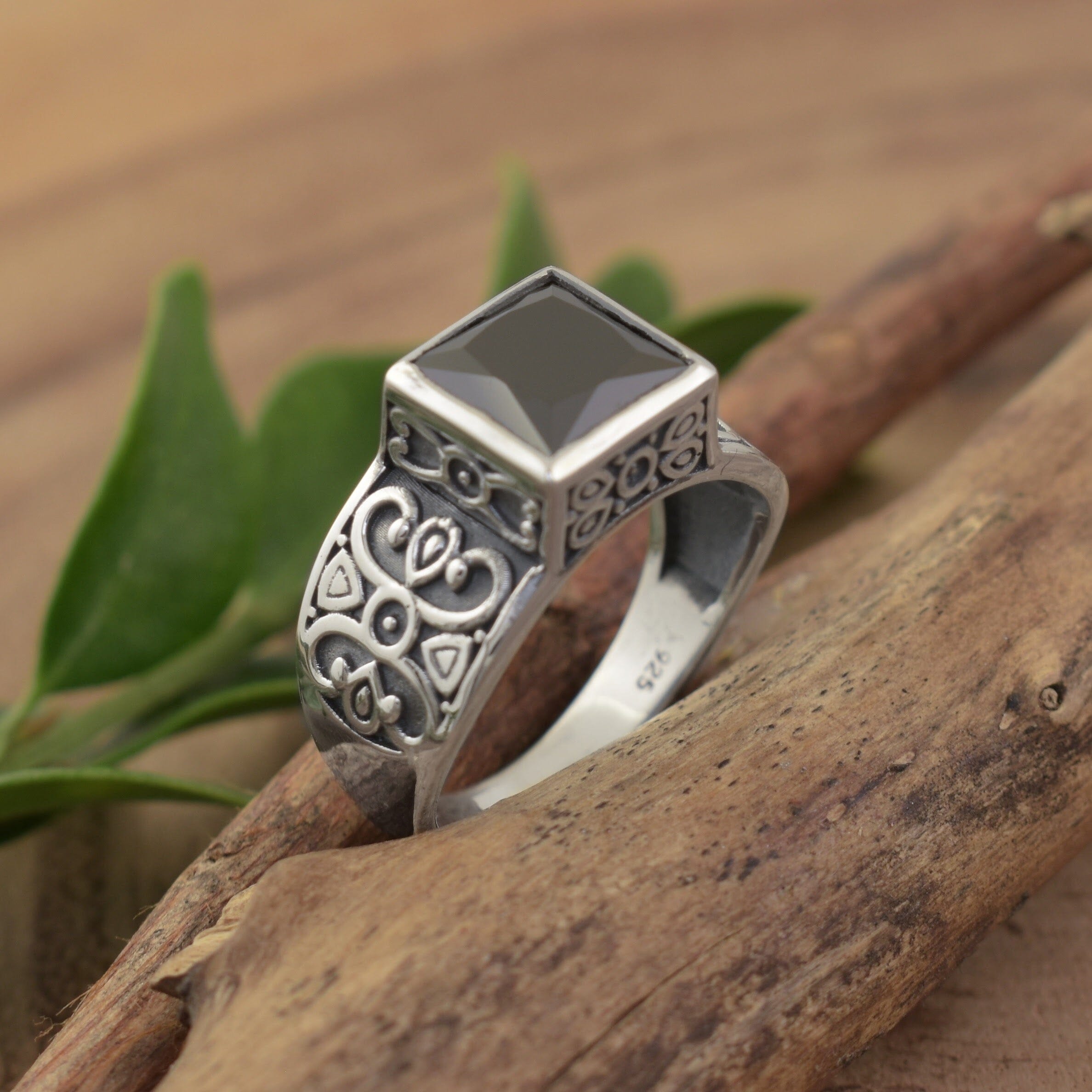 A sterling silver ring with engraved scrollwork along the wide band, featuring a large black square CZ stone