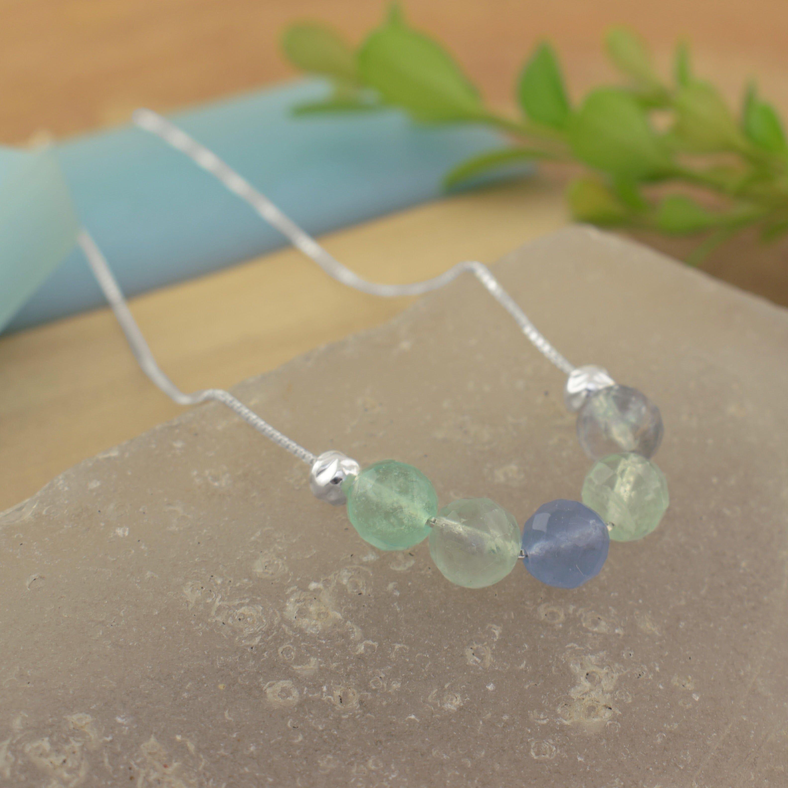 a finely crafted delicate sterling silver necklace with five faceted beads in light green, pale blue, and frosted white