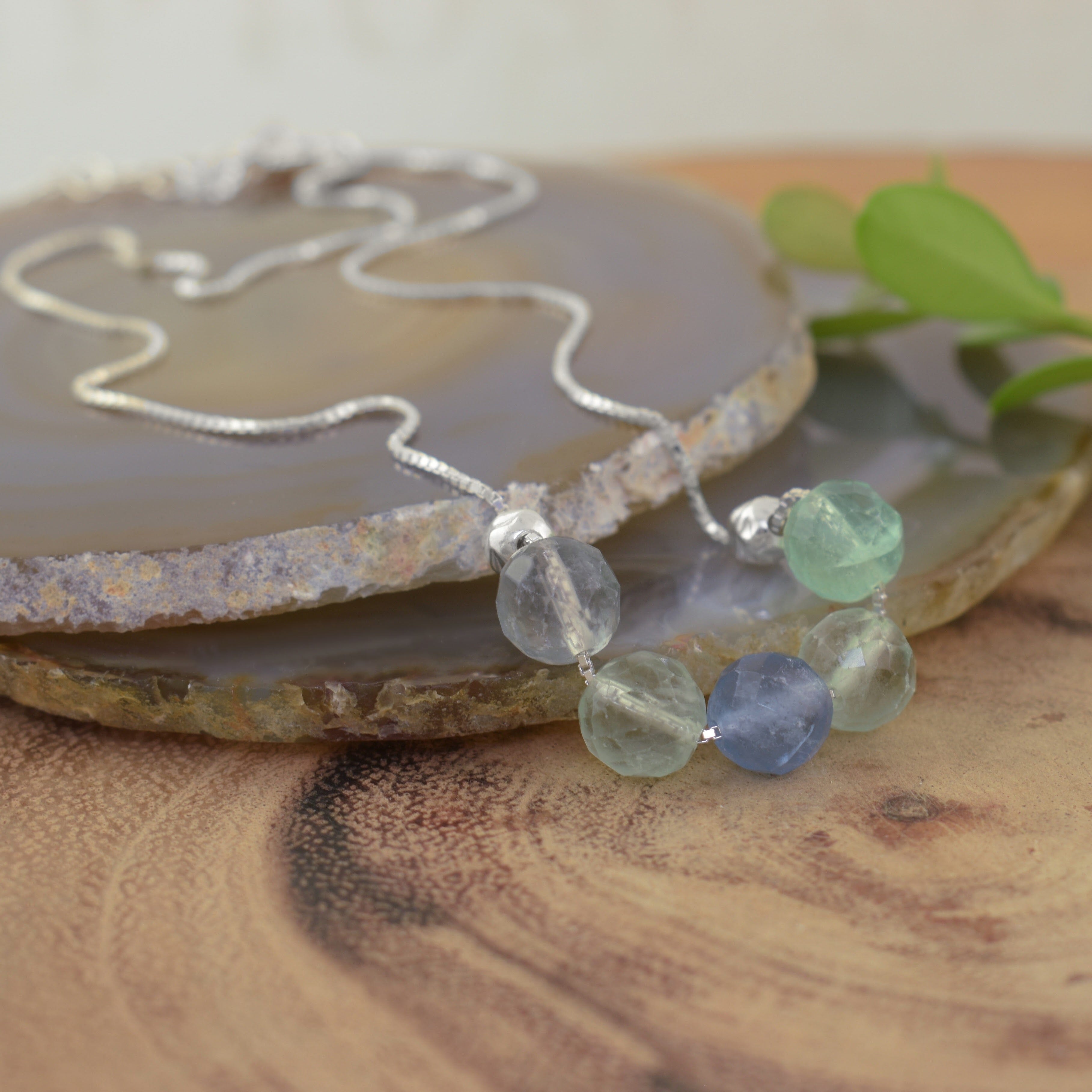 a sterling silver necklace chain with five faceted gemstone beads in light green, blue, and clear