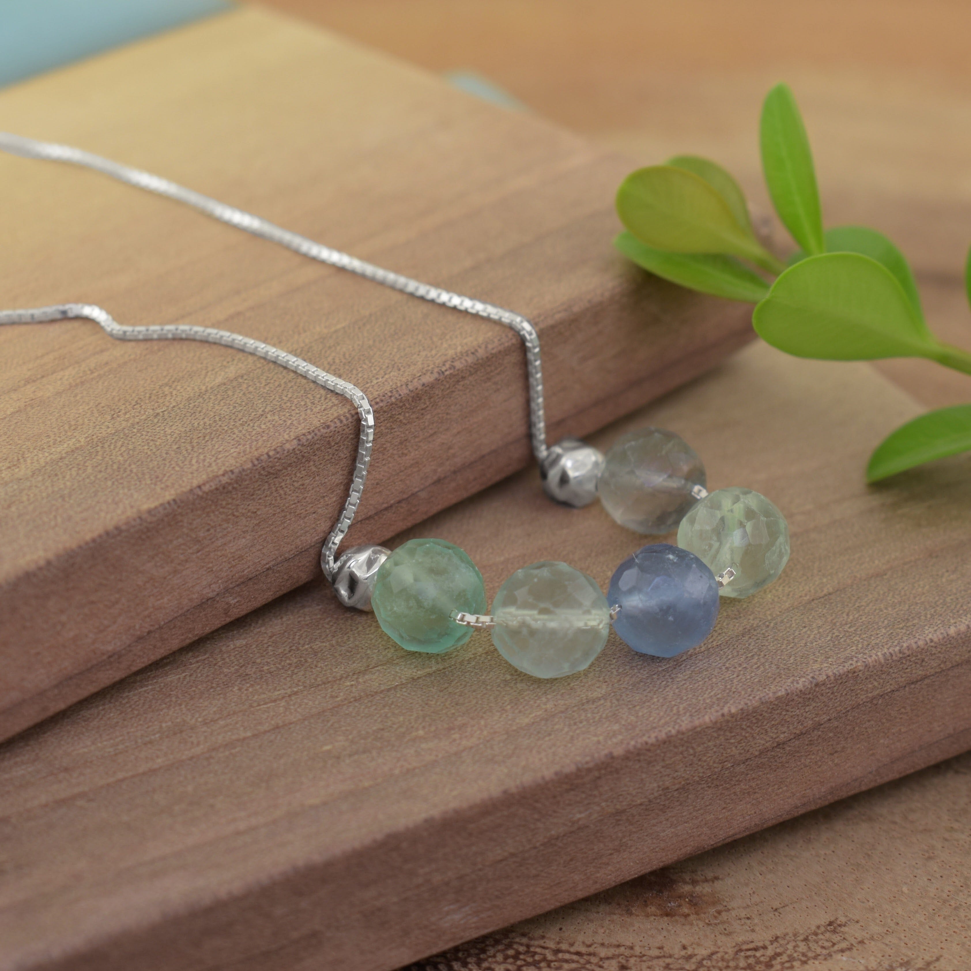 a sterling silver necklace chain with five faceted beads in light green, pale blue, and frosted white