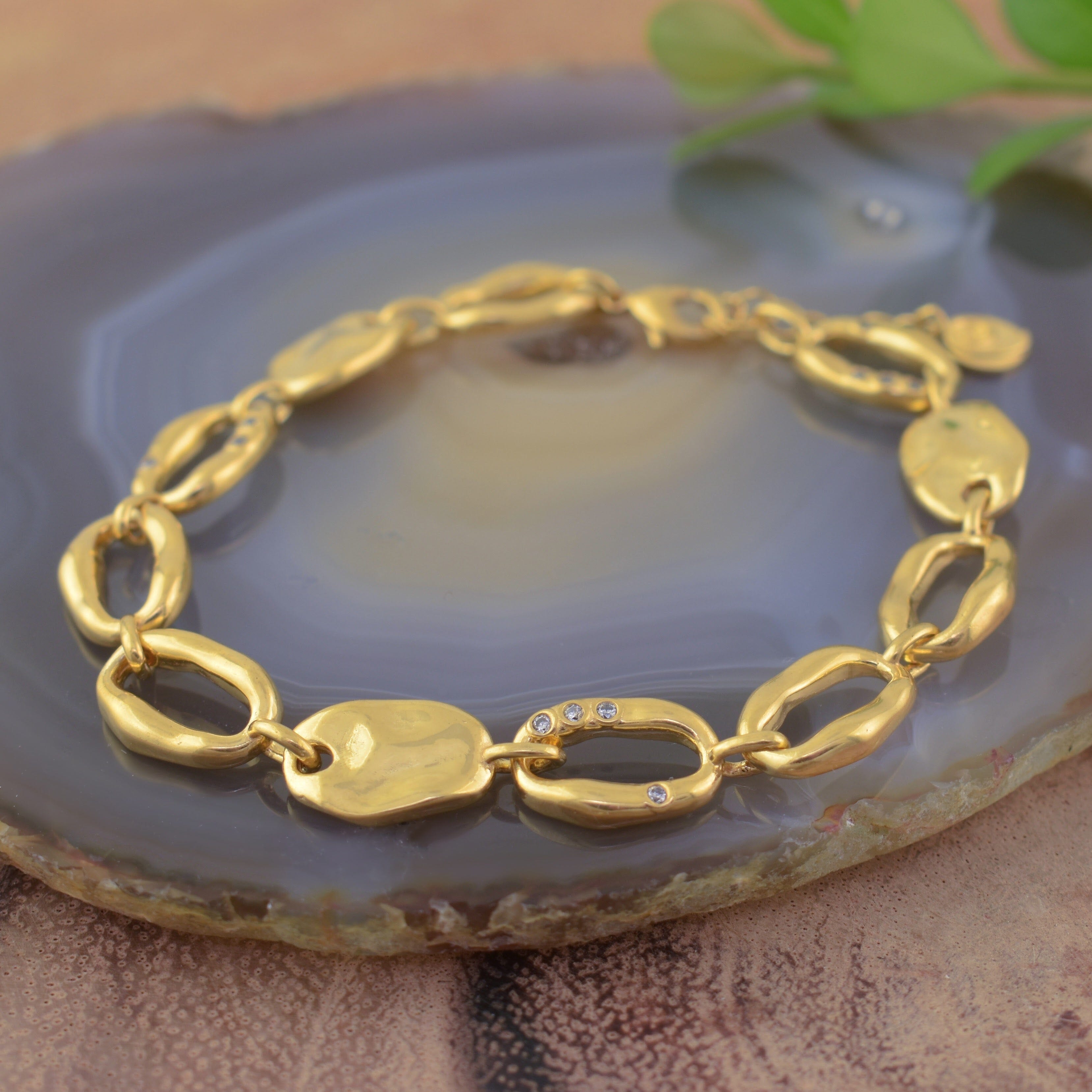a polished gold-plated link bracelet with organic-shaped oval links and tiny CZ stones scattered on the chain links