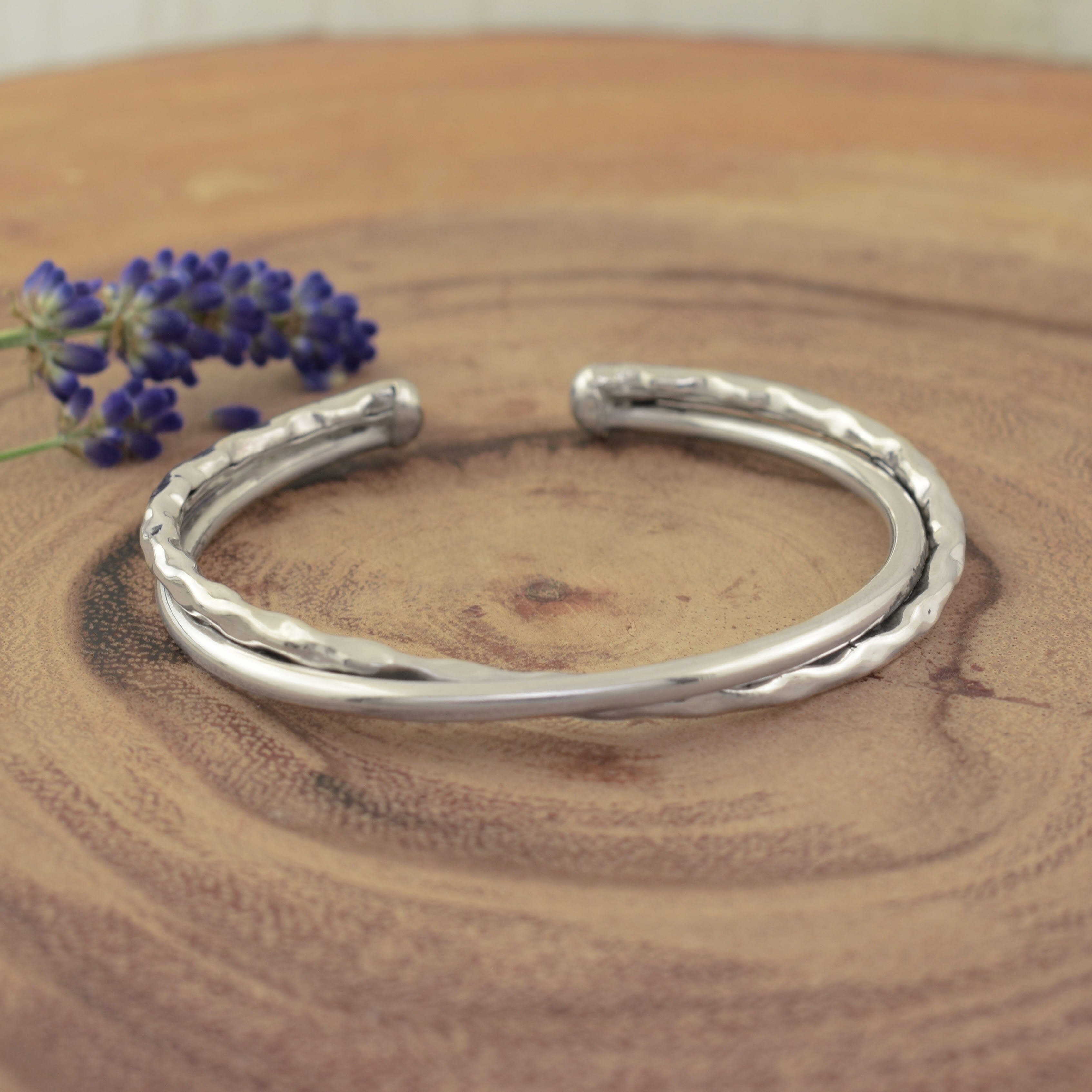 A sterling silver cuff bracelet featuring two intertwining bands with one band hammered and the other smooth