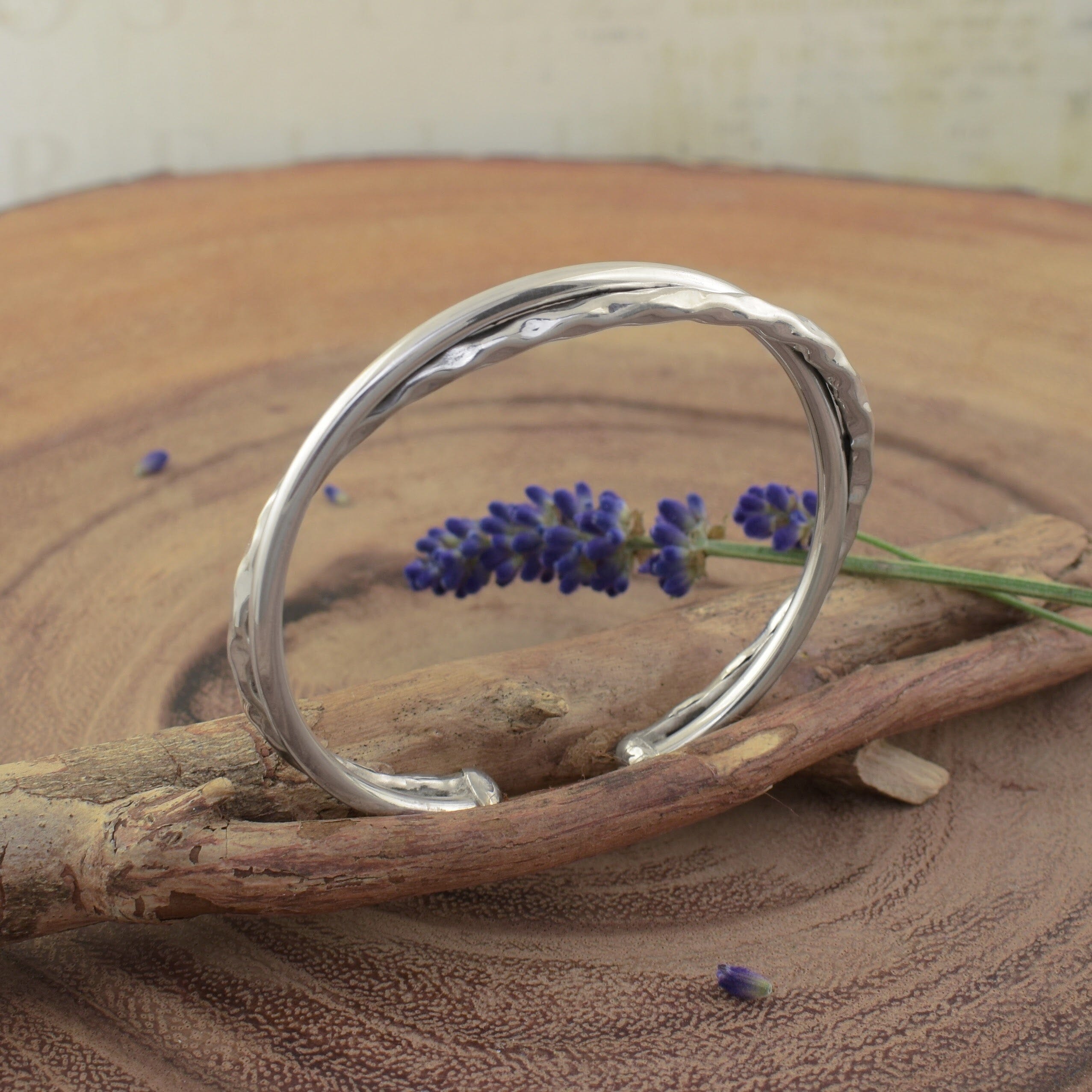 A sterling silver cuff featuring two intersecting bands, with one band a smooth finish and the other hammered