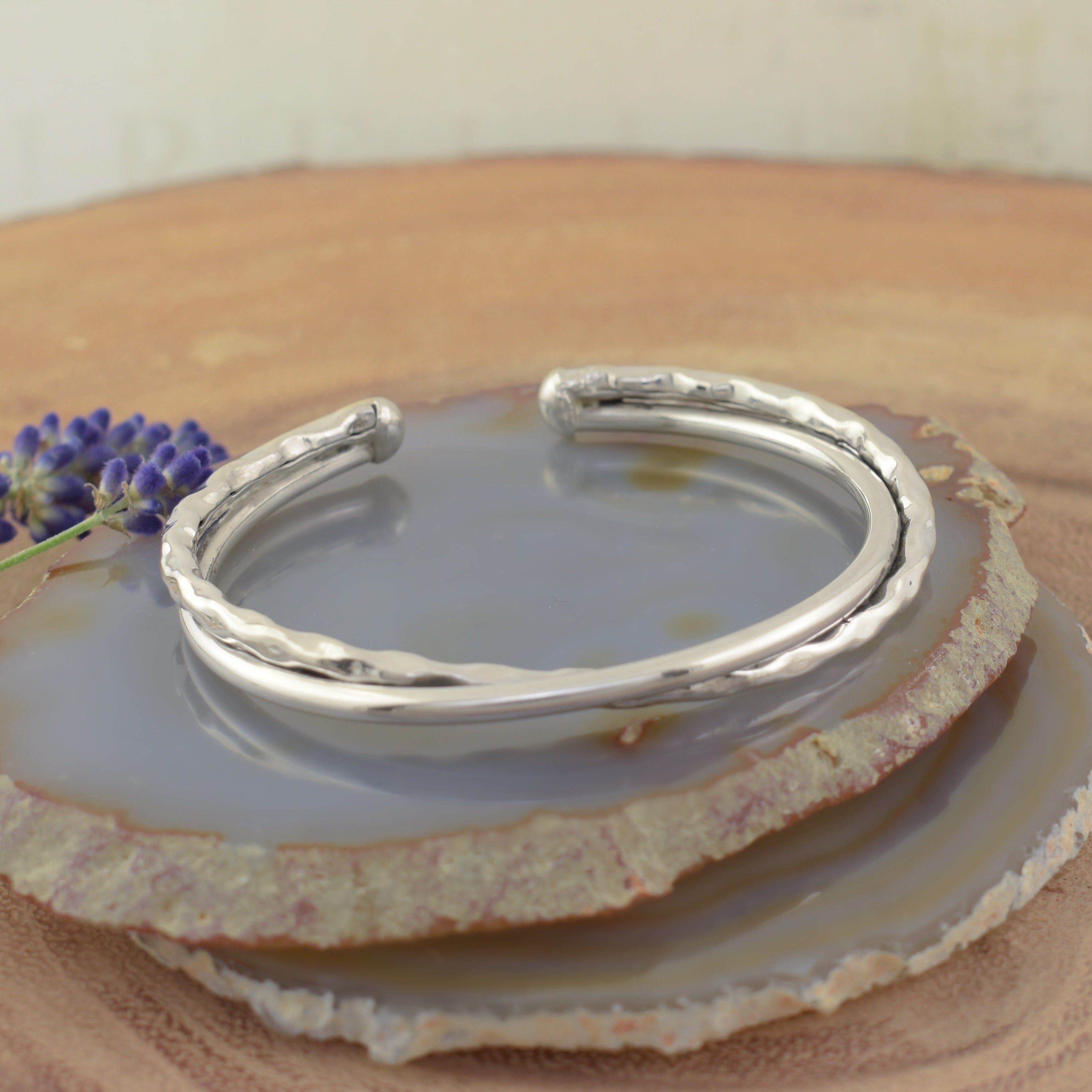 A sterling silver cuff bracelet with two bands curling around each other, with one band a hammered finish and the other smooth